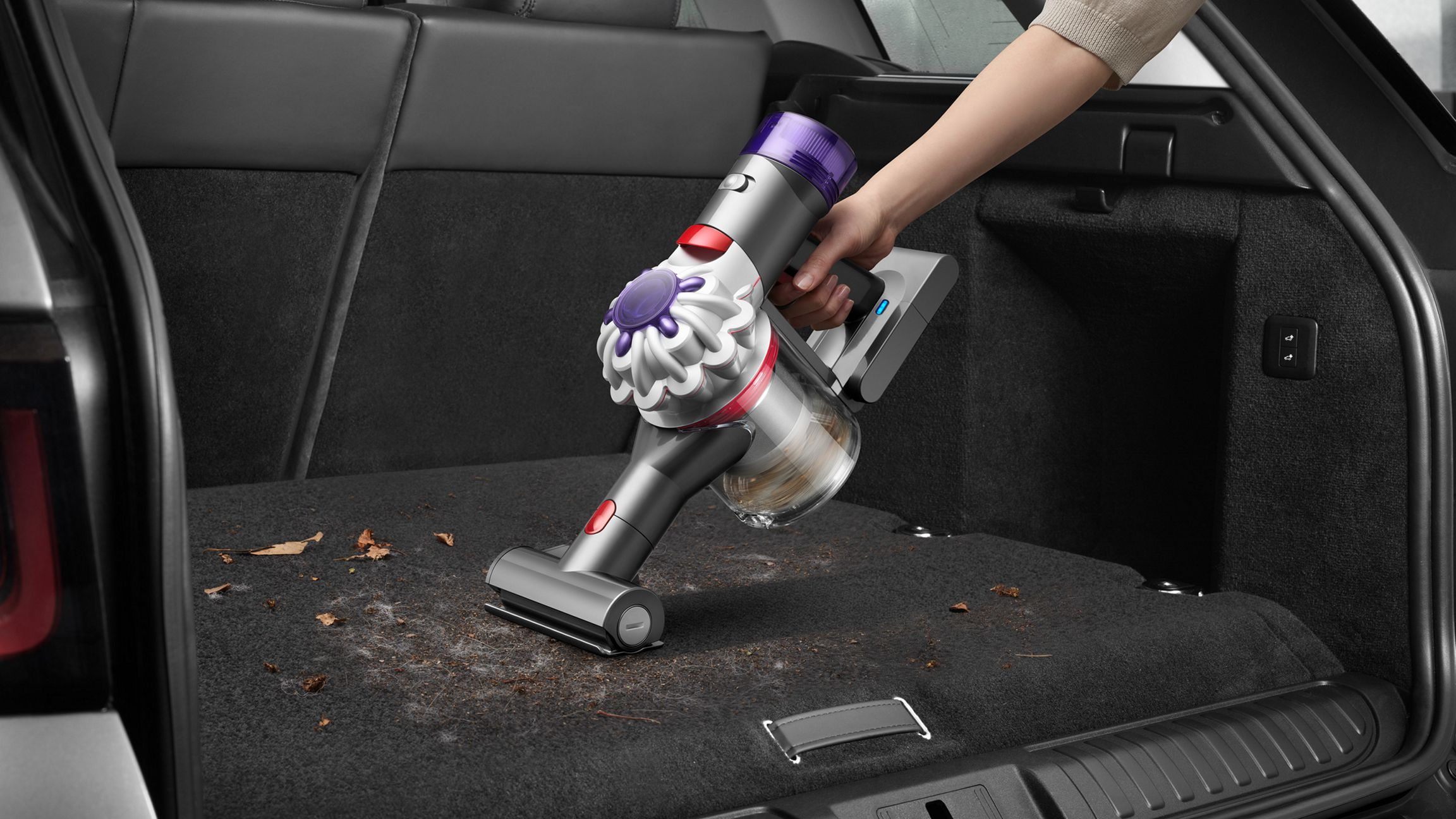 Personne passant l'aspirateur dans le coffre d'une voiture avec un aspirateur à main.