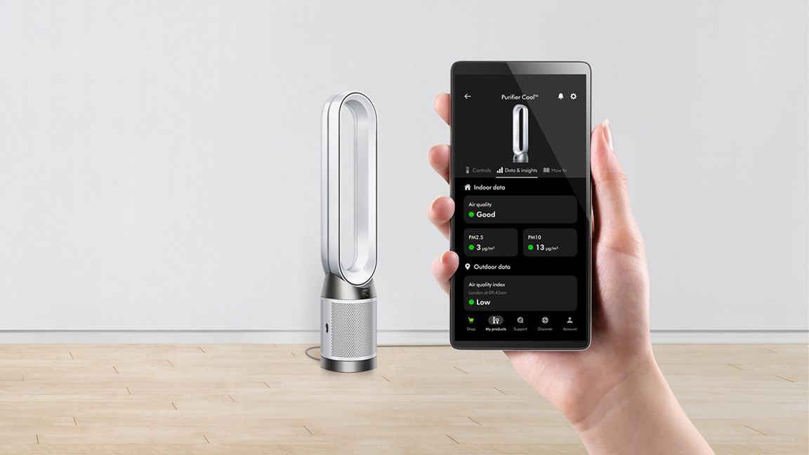 Purificateur d'air Dyson et téléphone affichant les données de qualité de l'air, sur un sol en bois.