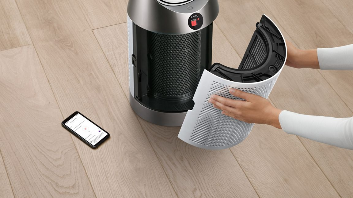 Mains d'une personne retirant un filtre d'un purificateur d'air blanc.