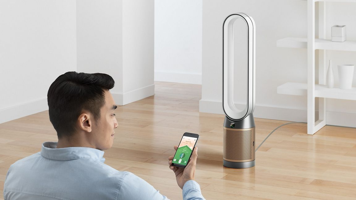 Homme utilisant un smartphone pour contrôler un ventilateur Dyson. Le ventilateur est sur un sol en bois.