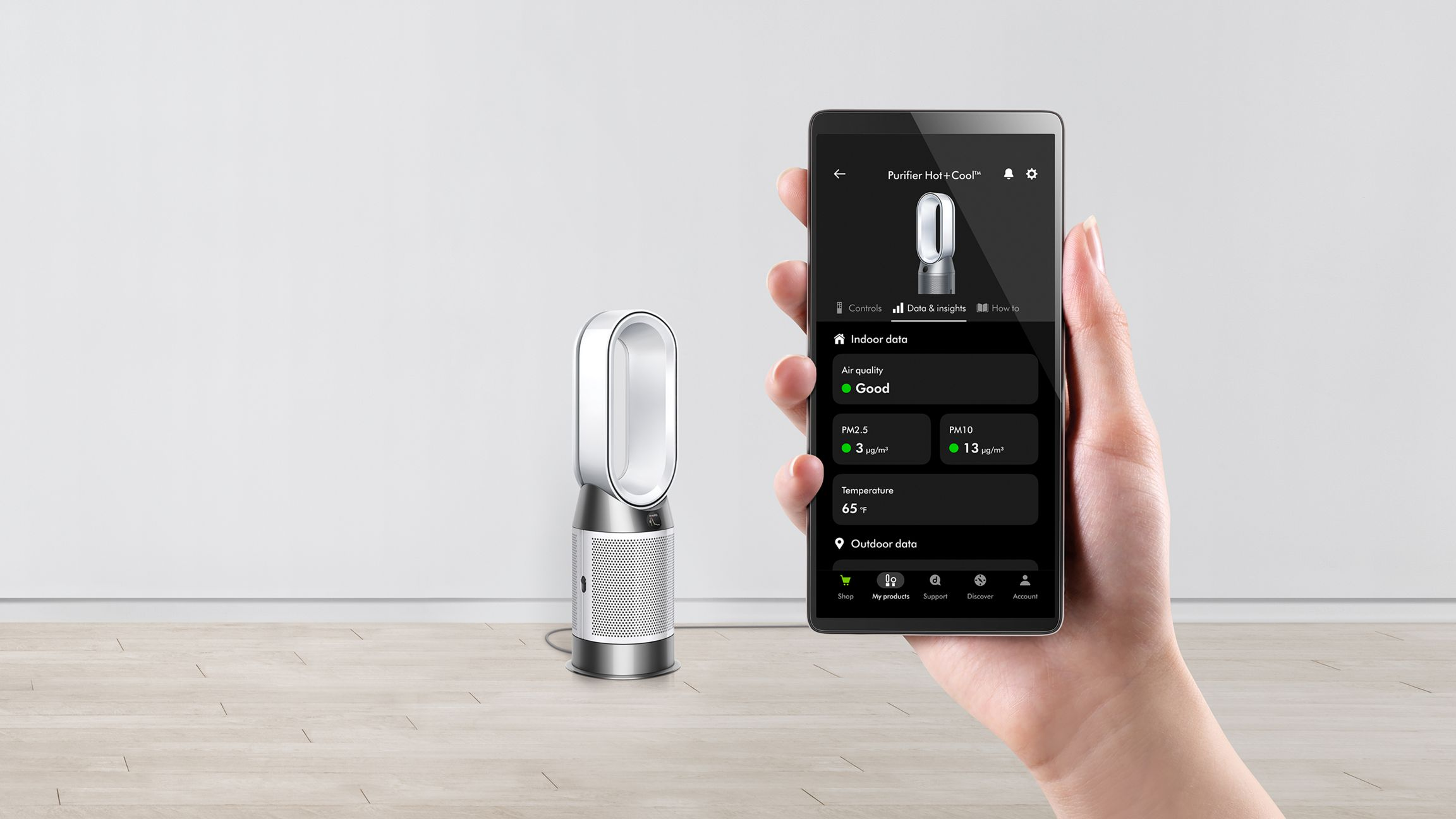 Une personne tient un téléphone affichant l'interface d'un purificateur d'air Dyson à côté du purificateur.