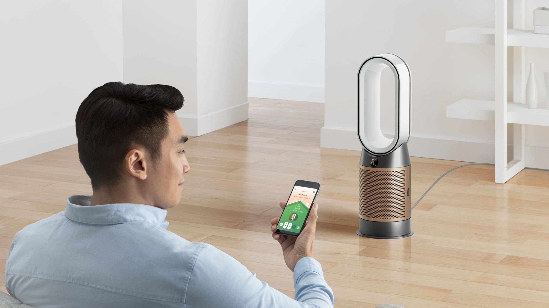 Homme tenant un téléphone, ventilateur Dyson en arrière-plan, plancher bois.