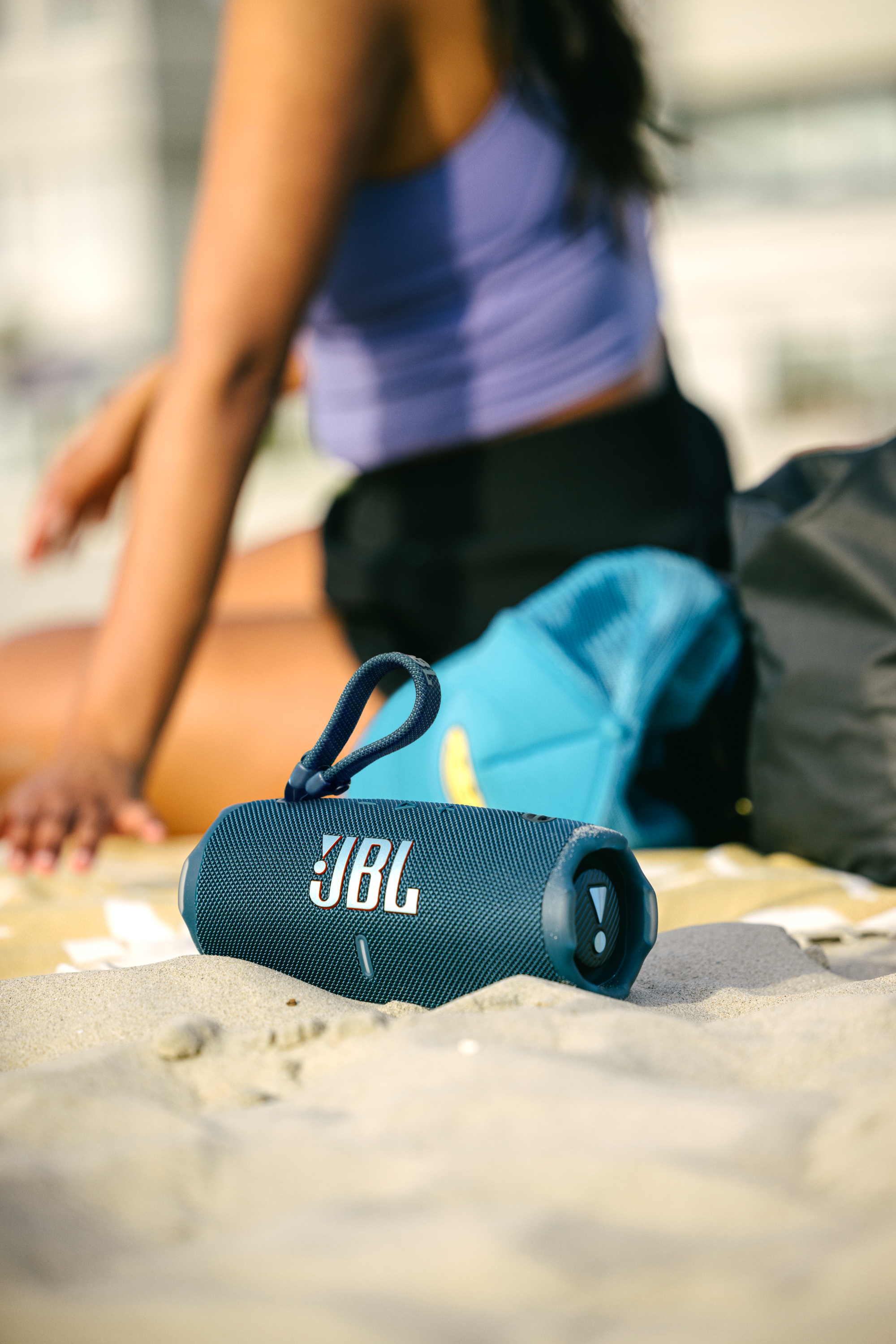 Kum üzerinde bir JBL hoparlör ve arka planda bir kişi.
