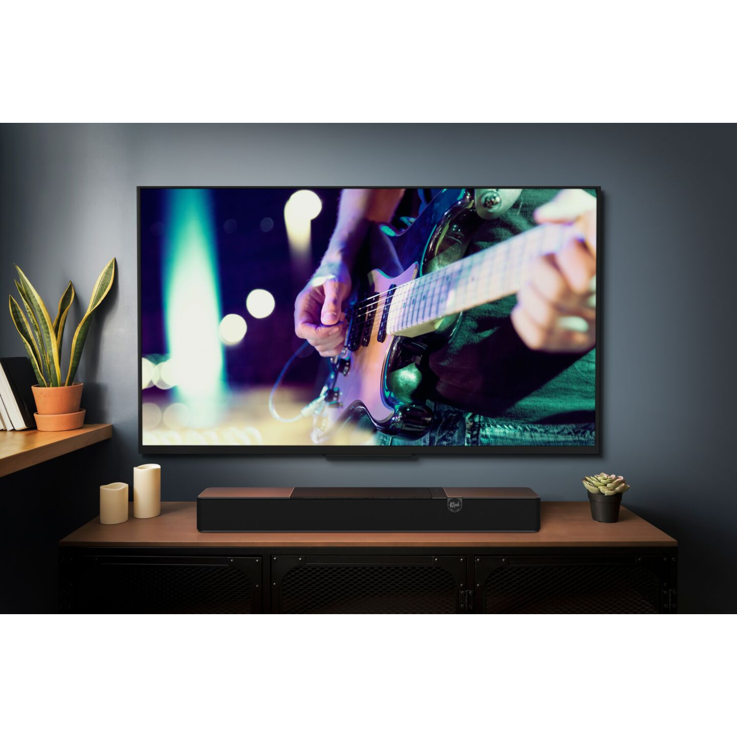 Een grote tv met een persoon die gitaar speelt op het scherm, soundbar eronder.