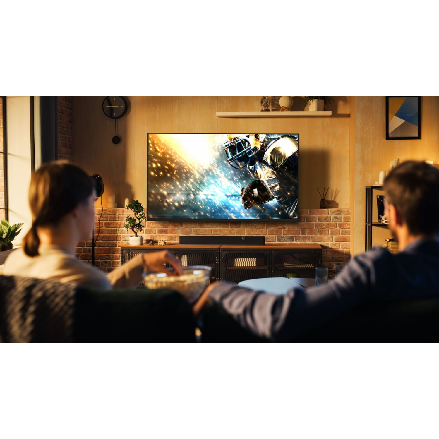 Twee mensen kijken tv. De tv toont een American football wedstrijd. Soundbar onder de tv.