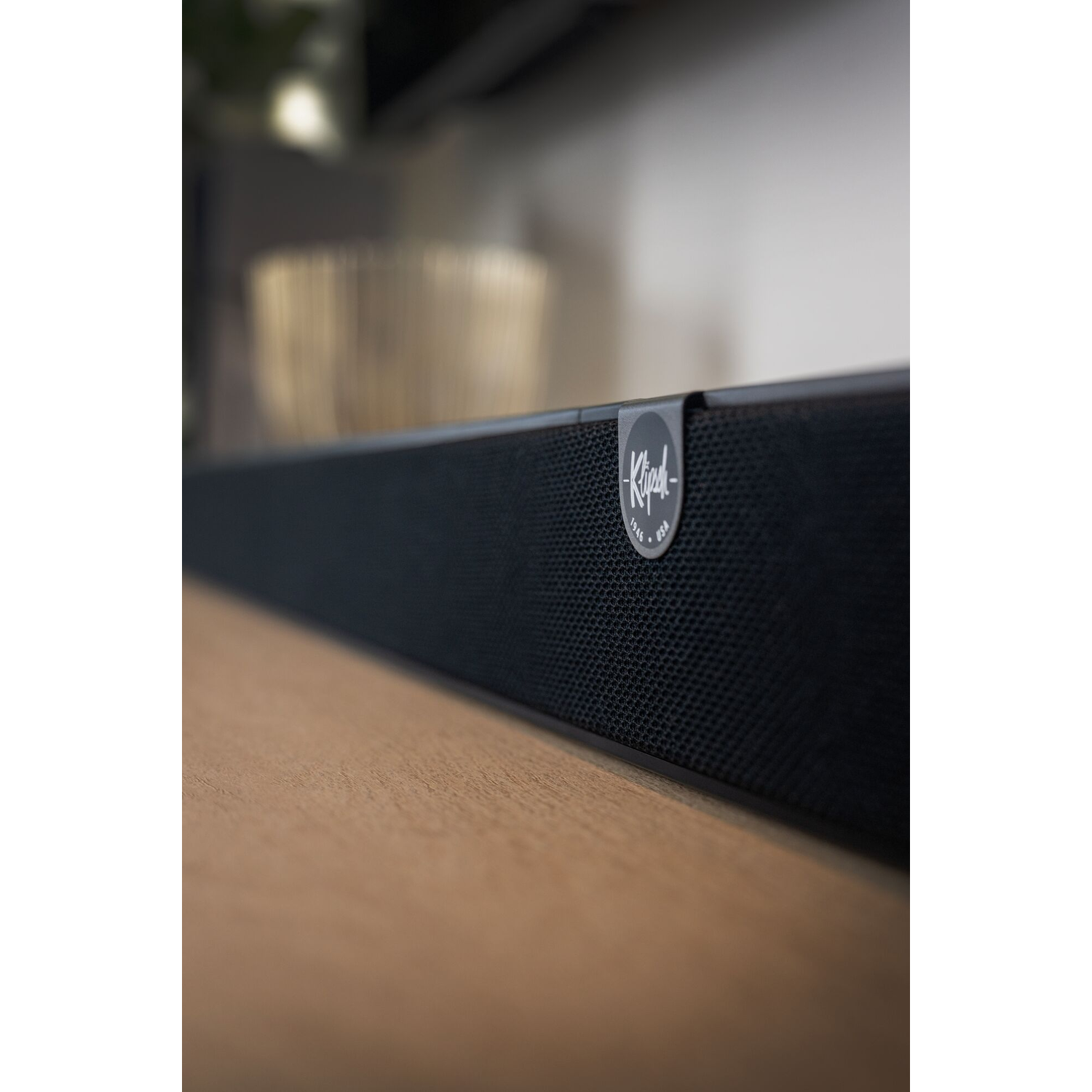 Zwarte soundbar op houten oppervlak, met Klipsch-logo, wazige achtergrond.