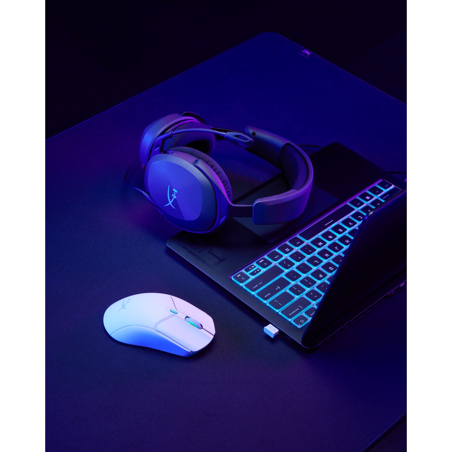 Gaming setup met headset, toetsenbord, muis op zwart oppervlak, met blauwe en paarse verlichting.