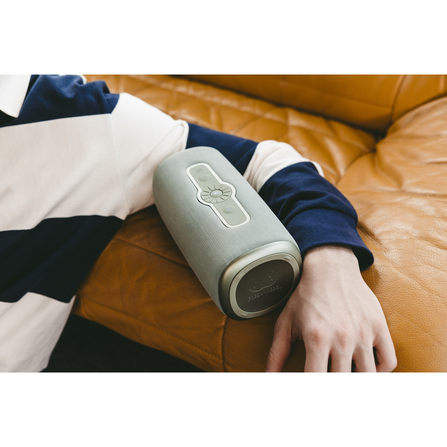 A person's arm holding a grey speaker on a leather couch.