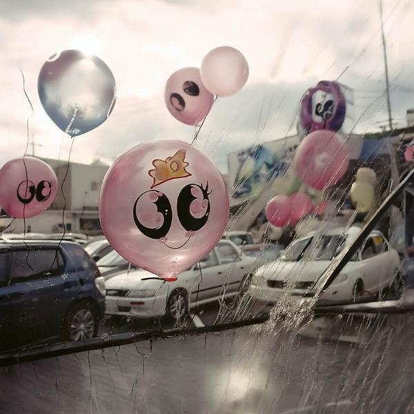 Ballons mit Gesichtern, die an einem Regentag vor Autos schweben.