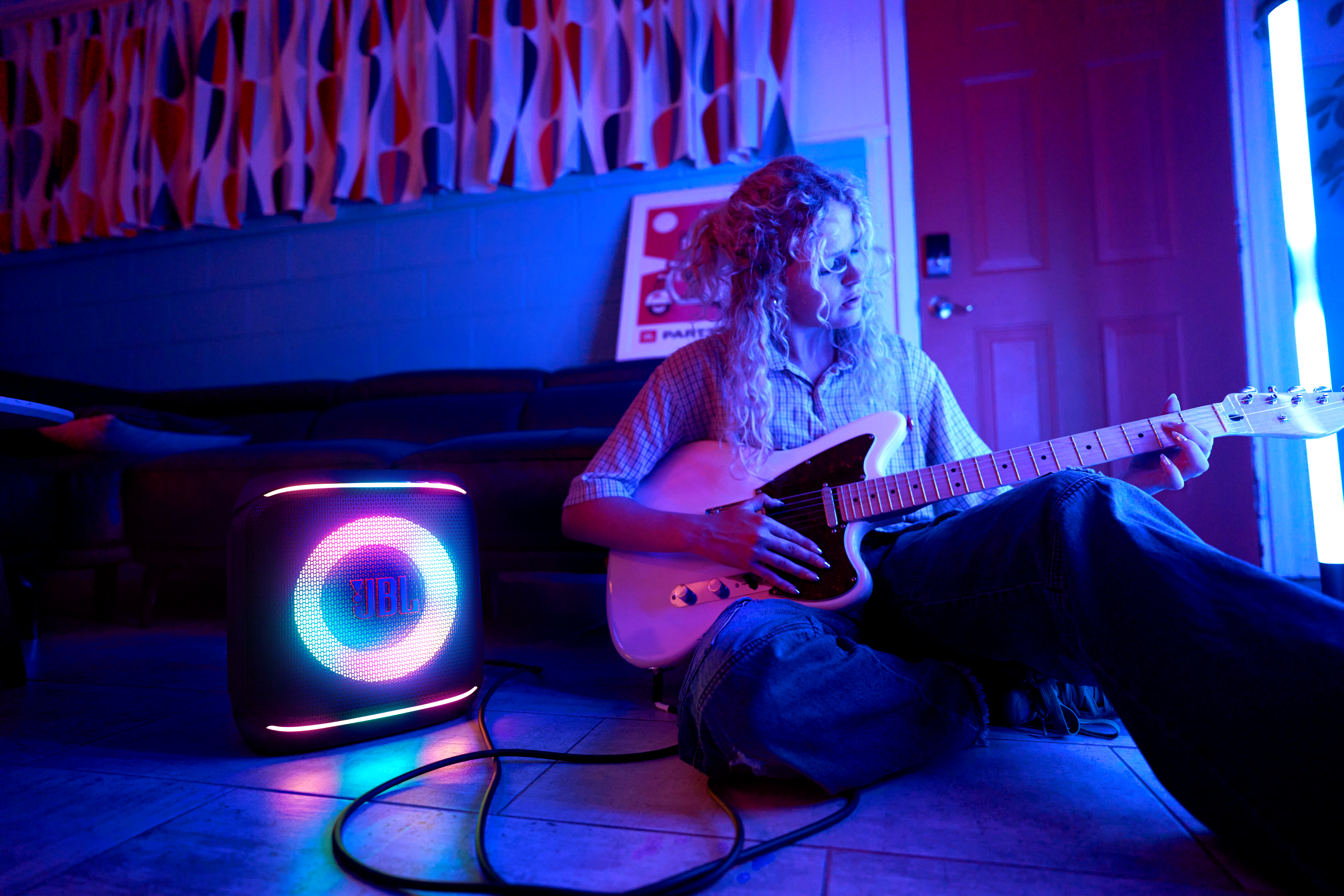 Renkli bir hoparlör ve neon ışıklarla dolu bir odada gitar çalan kadın.