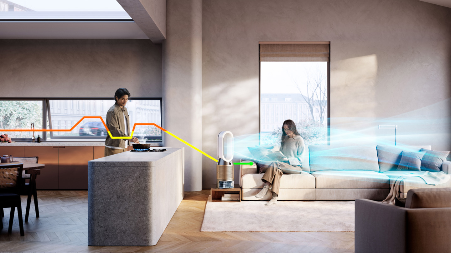 Mężczyzna gotuje w kuchni, kobieta jest na sofie. Oczyszczacz powietrza Dyson jest pośrodku.