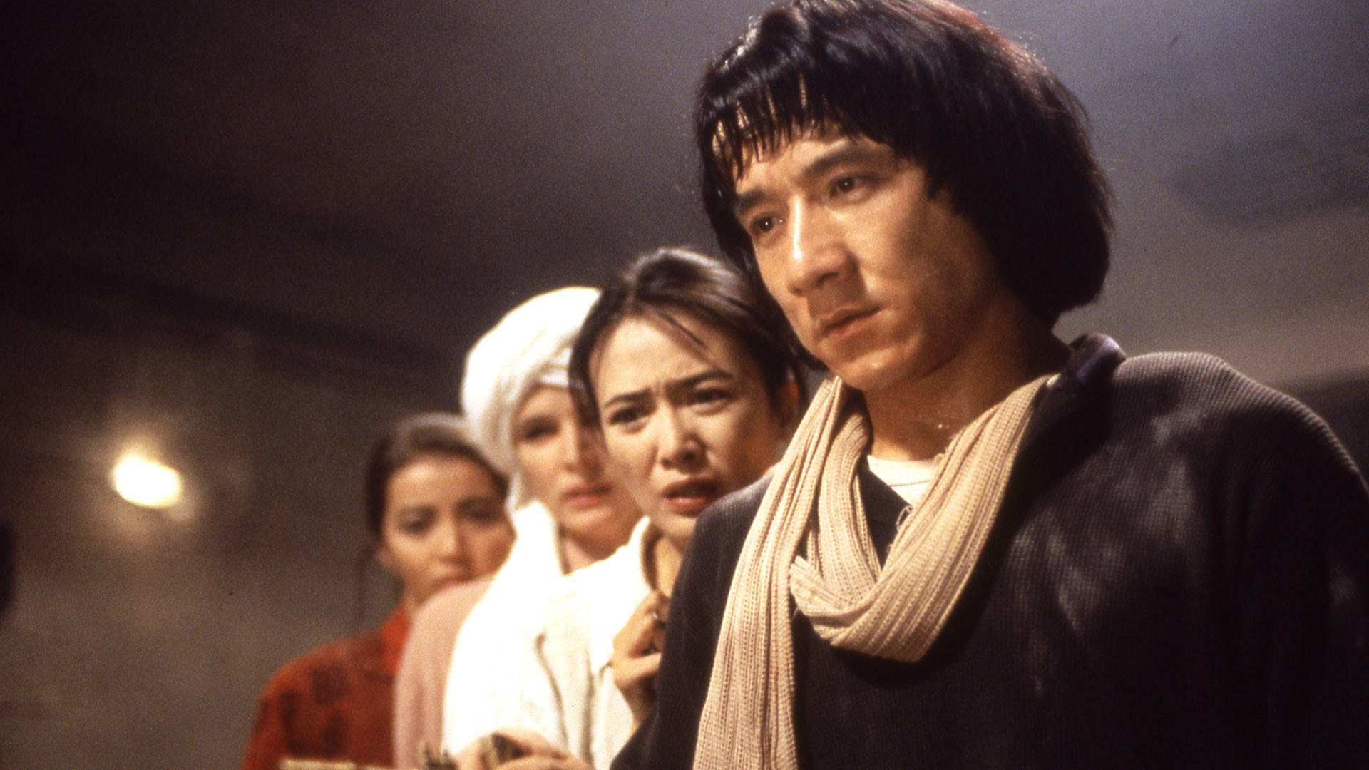 Jackie Chan und eine Gruppe von Leuten, die mit besorgten Ausdrücken etwas betrachten.
