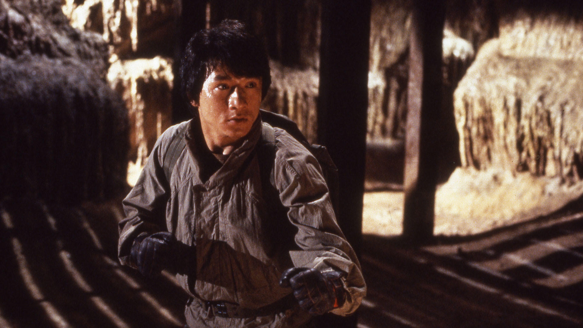 Jackie Chan in einer Höhle, blickt mit besorgtem Ausdruck in die Kamera.