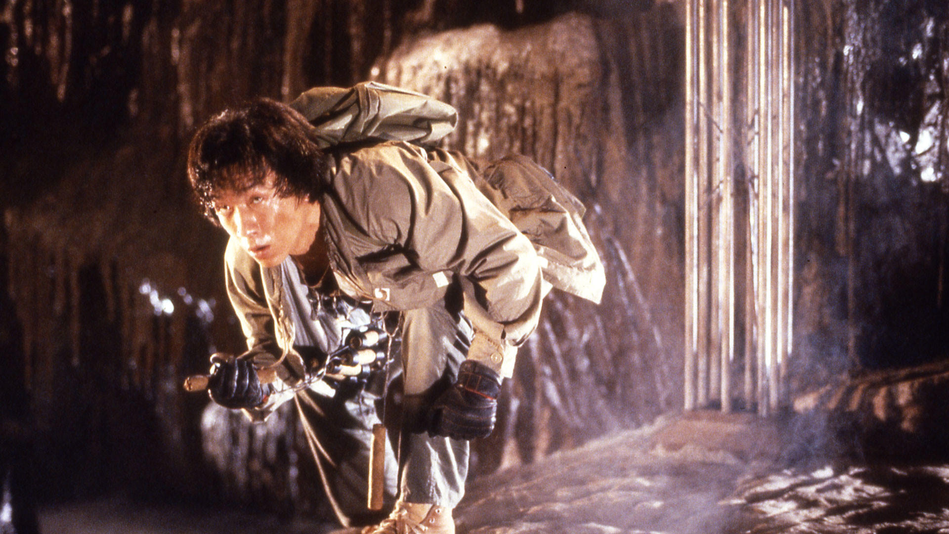 Ein Mann in einer Höhle blickt nach unten und hält eine Lampe. Er trägt einen Rucksack und Ausrüstung.