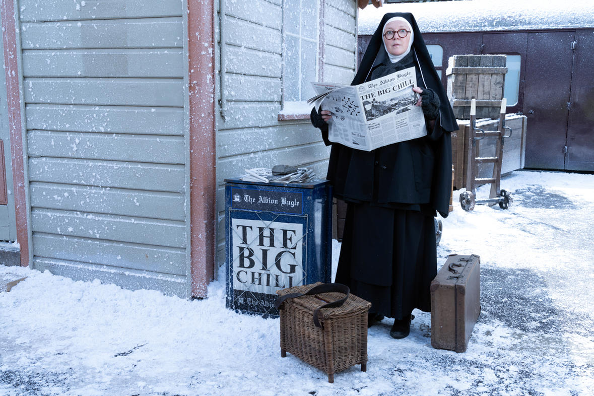 Nonne in schwarzem Habit liest Zeitung in verschneiter Szene.