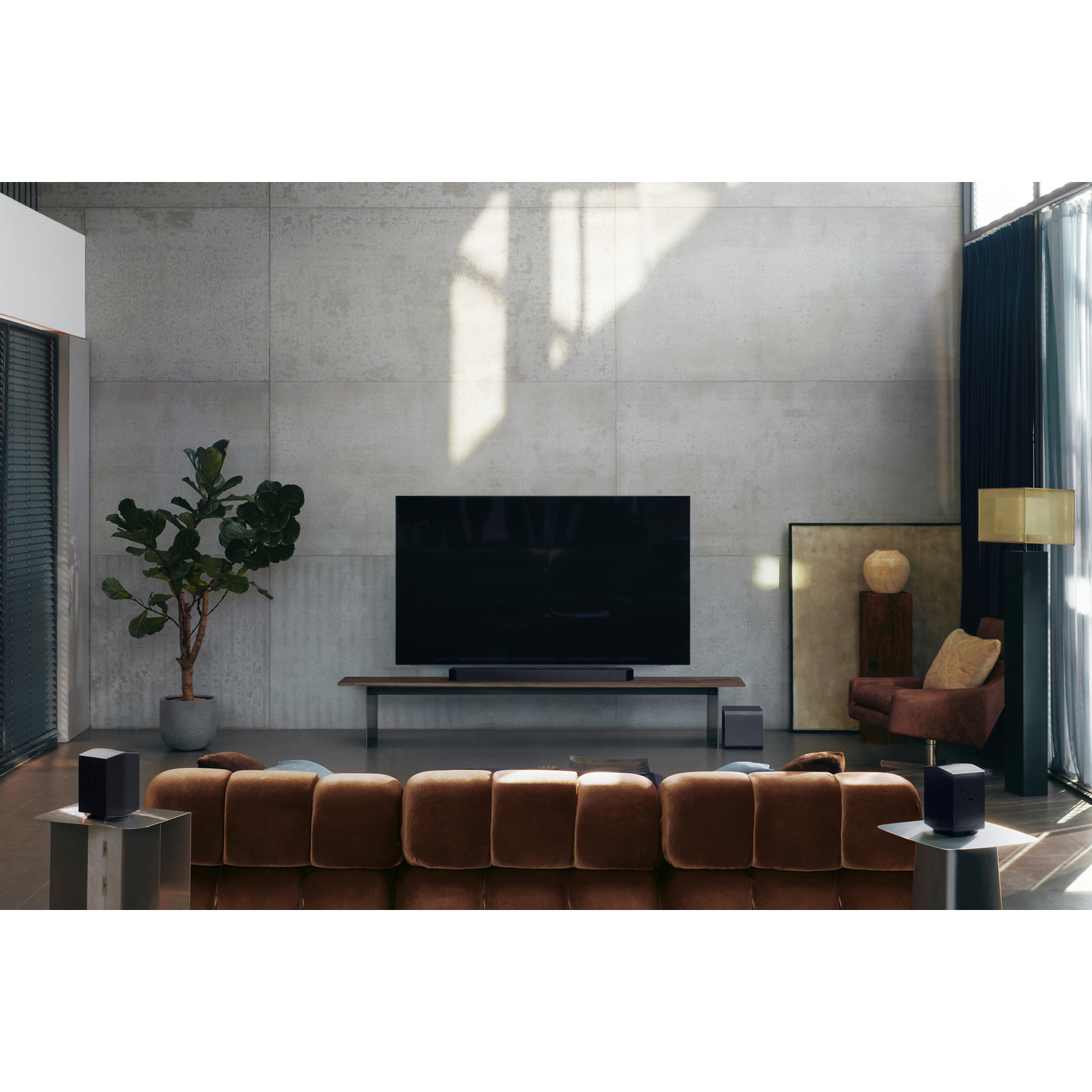 Een moderne woonkamer met een grote tv, soundbar, twee luidsprekers en een subwoofer. Bruine bank en betonnen muur.