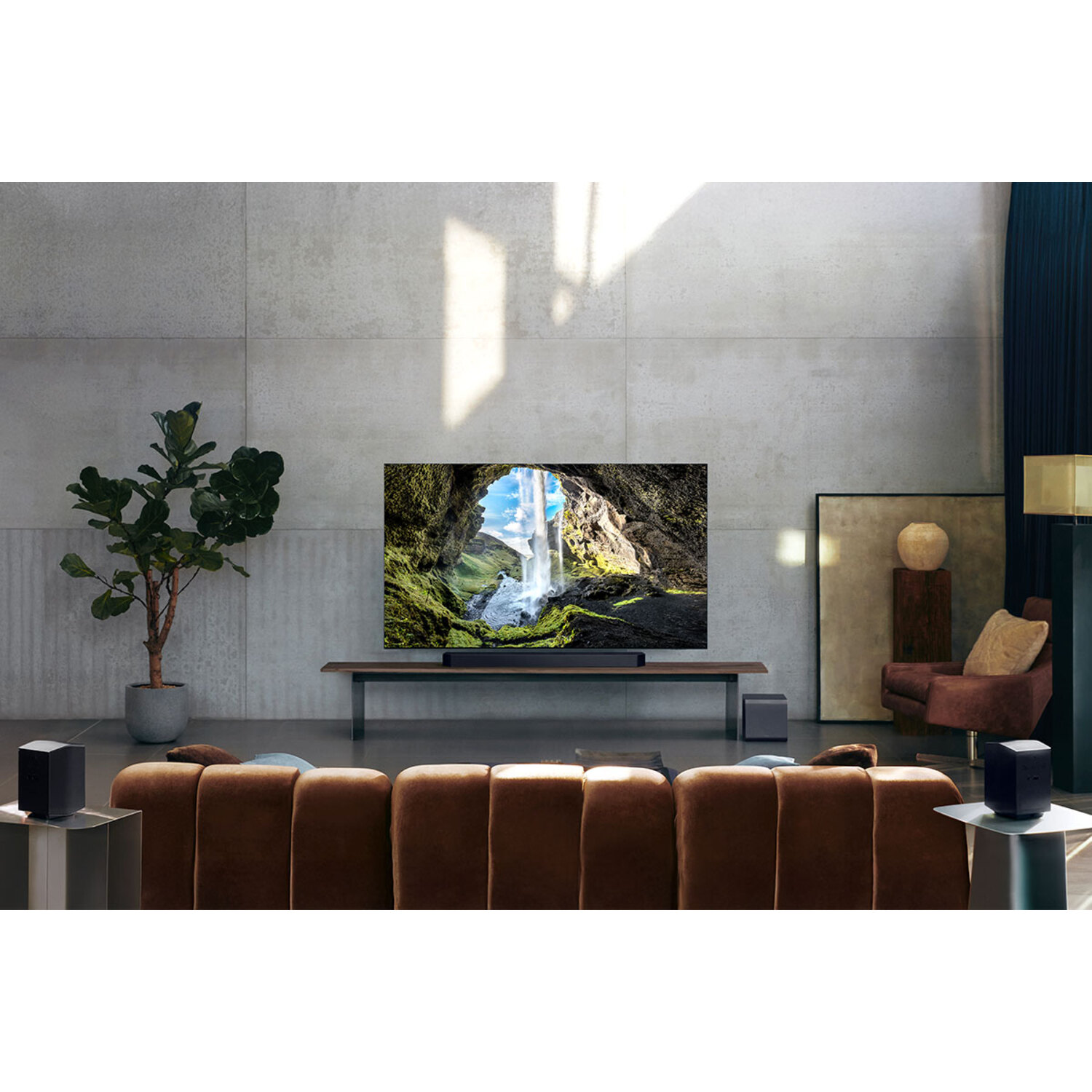 Woonkamer met een grote tv die een waterval toont. Bruine bank, zwarte luidsprekers, neutrale muren.