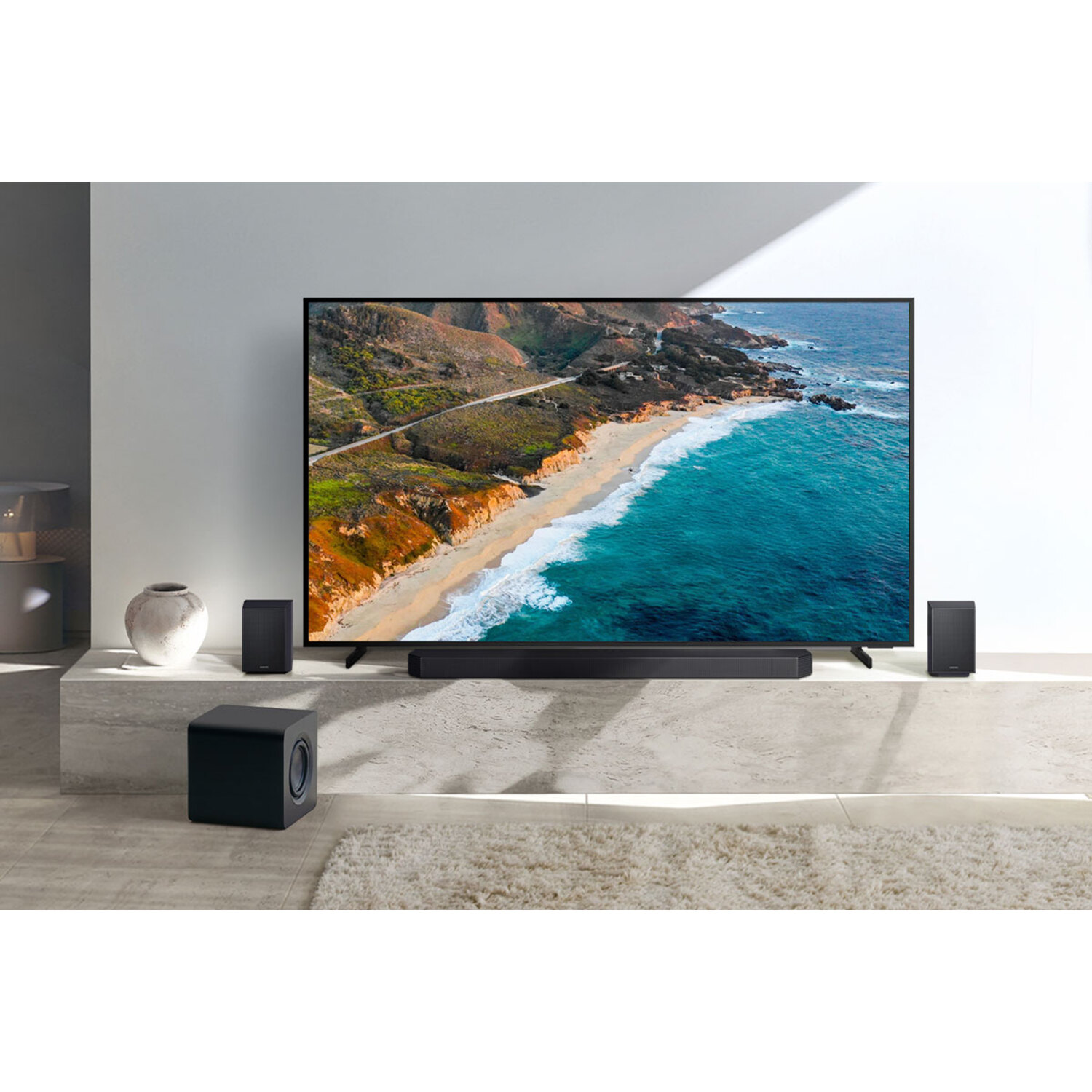 Une configuration de salon avec une TV, une barre de son, deux enceintes et un caisson de basses. La TV affiche une scène de plage.