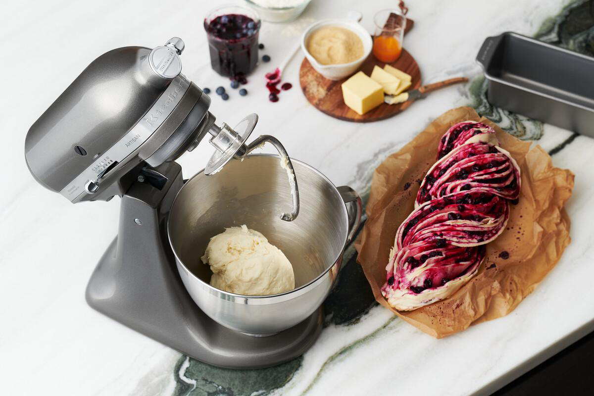 Grauer KitchenAid-Mixer mit Teig, Zutaten und Blaubeergebäck.
