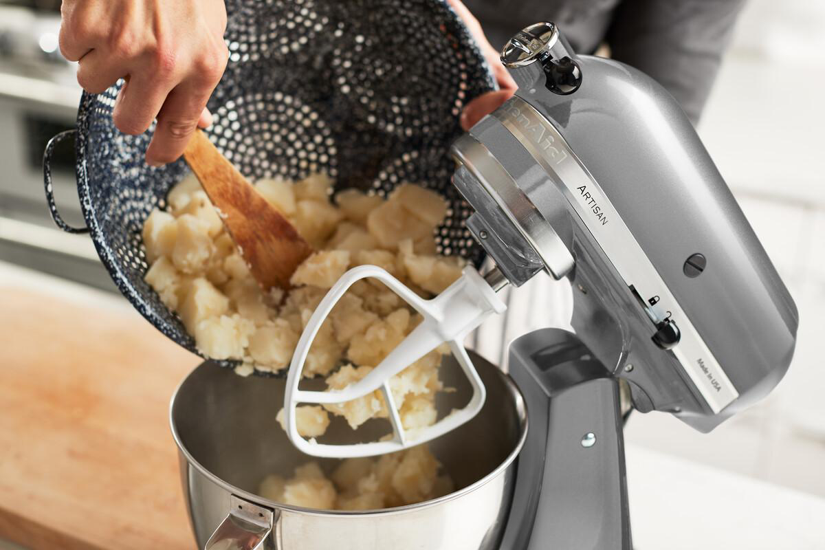 KitchenAid-Mixer mit Zugabe von Kartoffeln. Grauer Mixer, Holzlöffel, Schüssel.