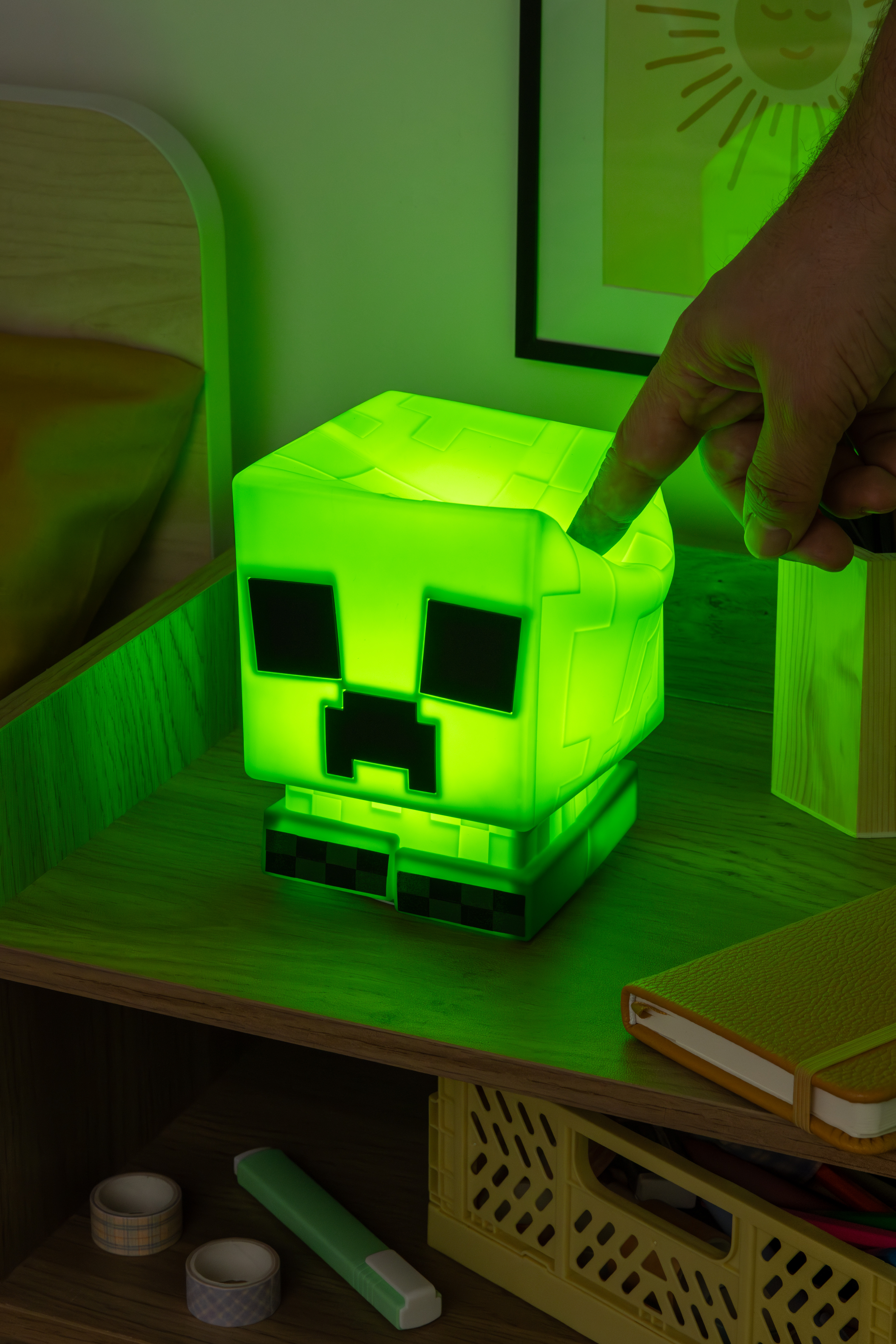 Grüne Minecraft Creeper-Lampe leuchtet auf einem Regal, mit einer Hand, die ihre Oberseite berührt.