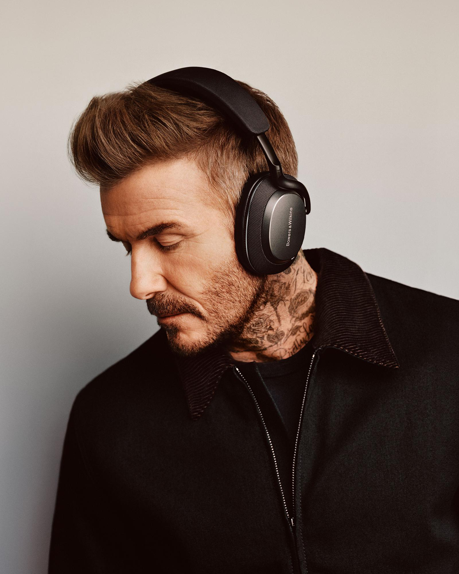David Beckham mit schwarzen Kopfhörern, Tattoos und ernstem Gesichtsausdruck.