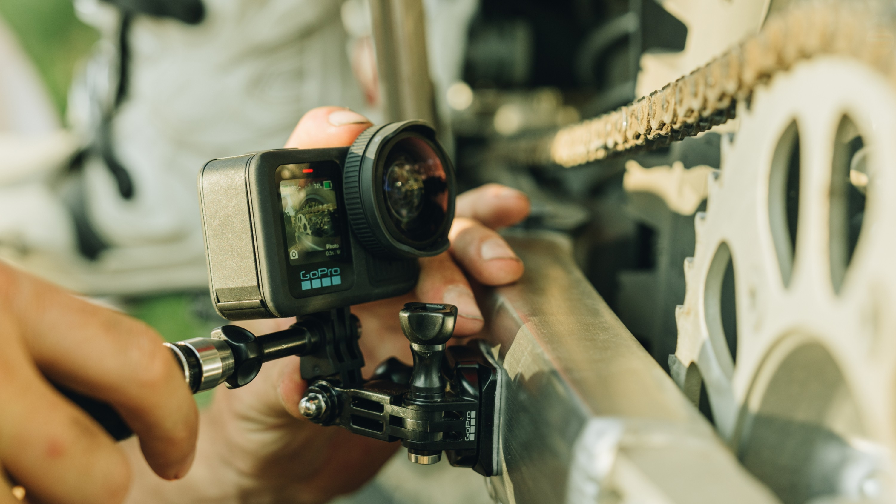 Person hält GoPro-Kamera an Fahrradteil, Kette im Hintergrund.