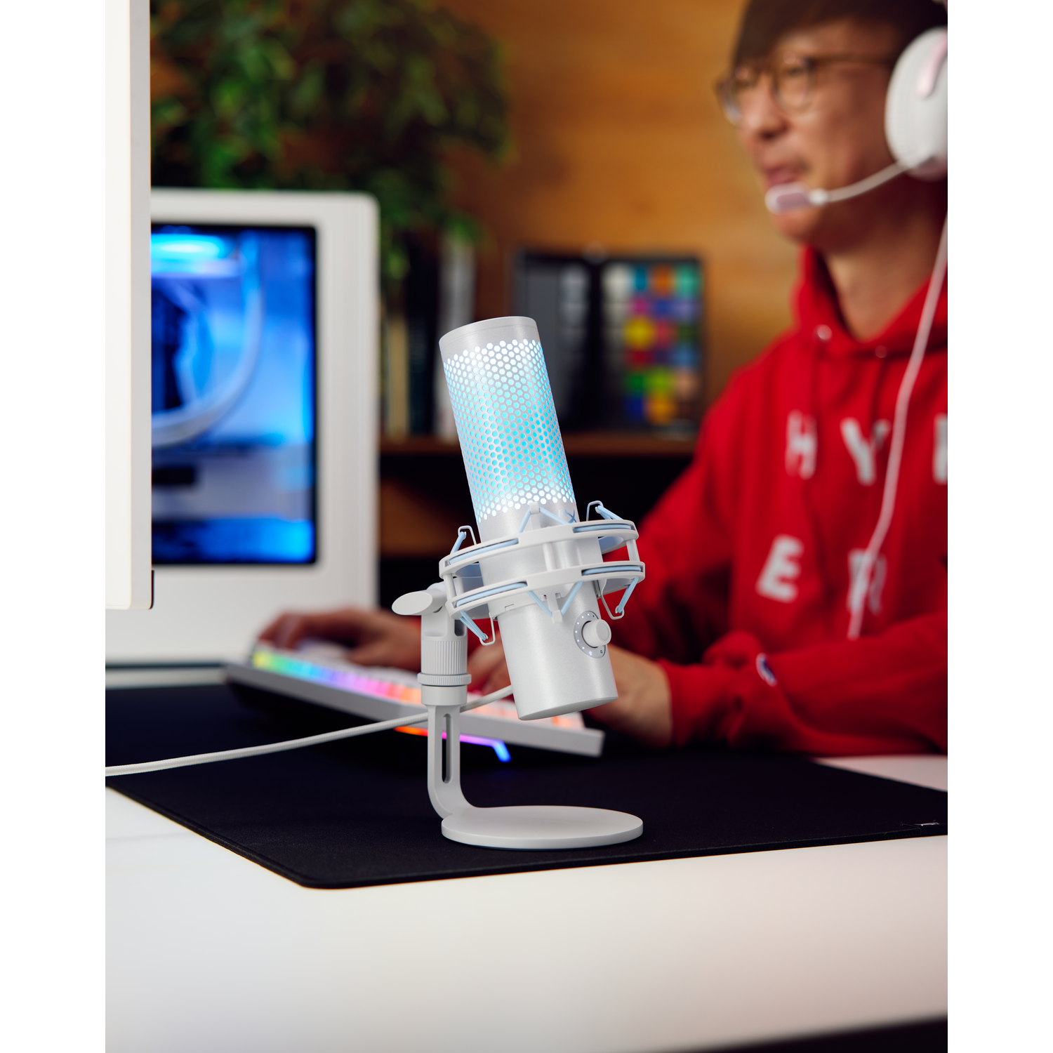 Een witte microfoon op een standaard met een gamer op de achtergrond.