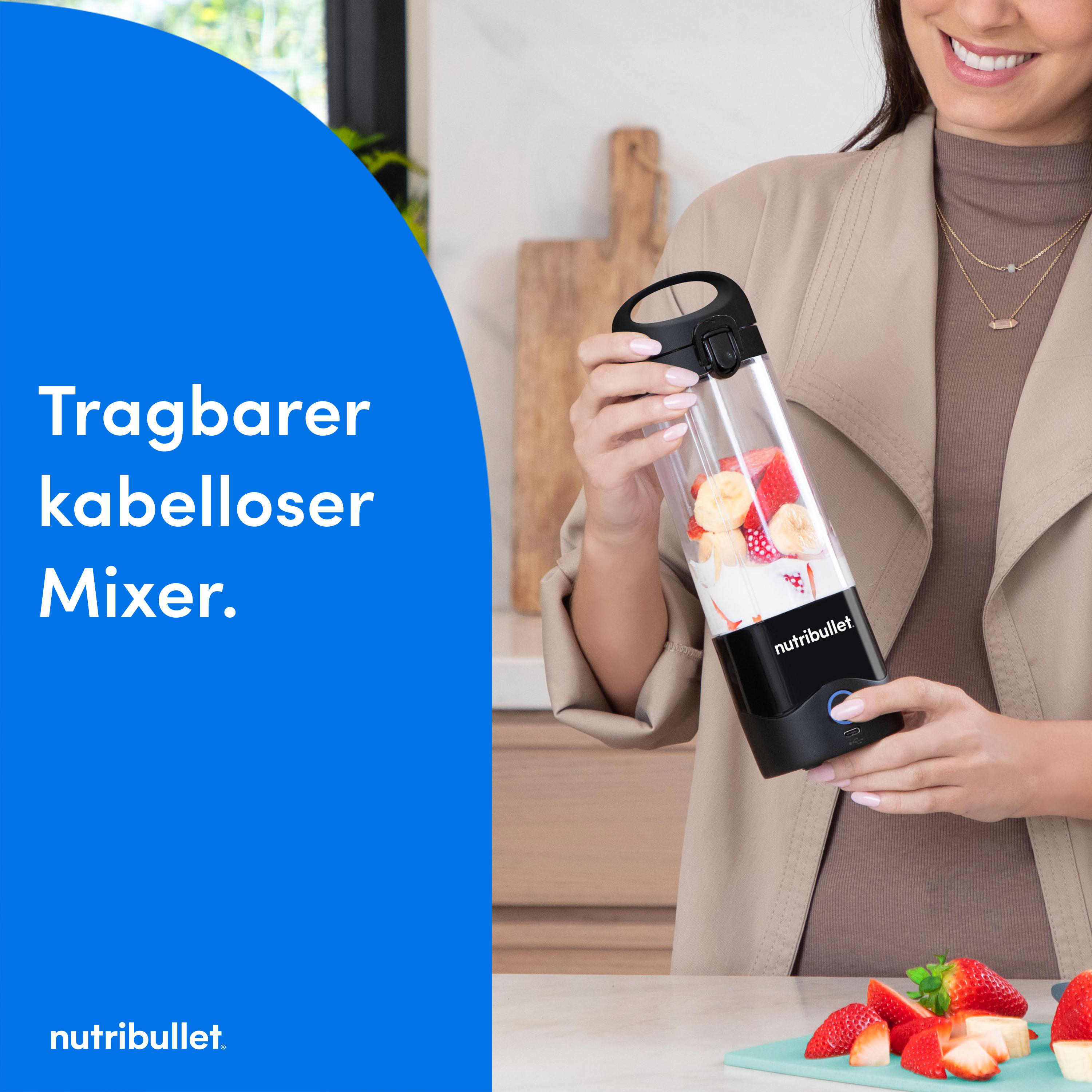Eine Frau hält einen tragbaren Mixer mit Früchten vor blauem Hintergrund.