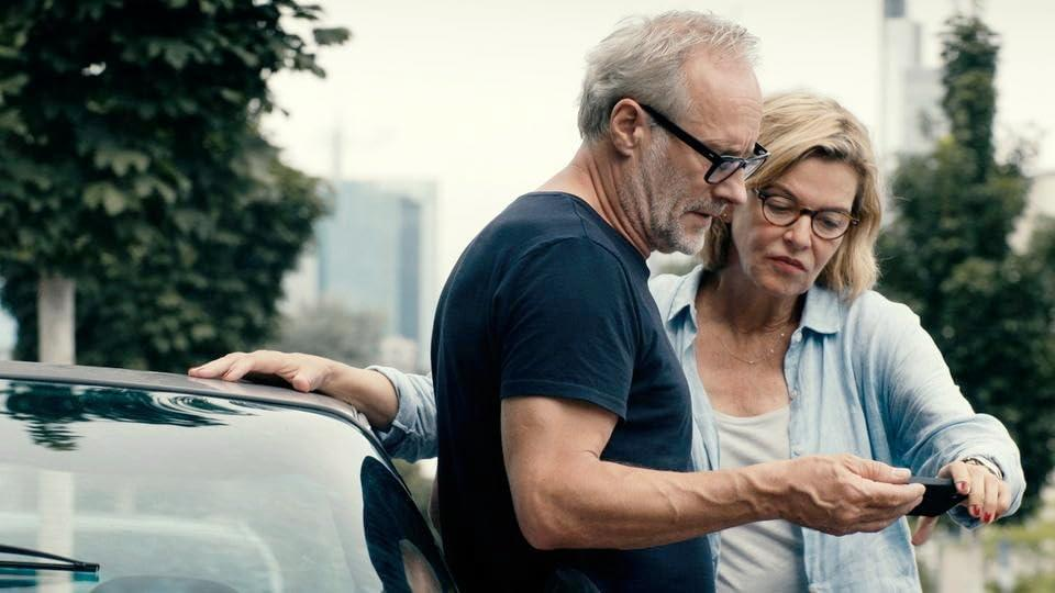 Ein Mann und eine Frau schauen sich in der Nähe eines Autos ein Telefon an.