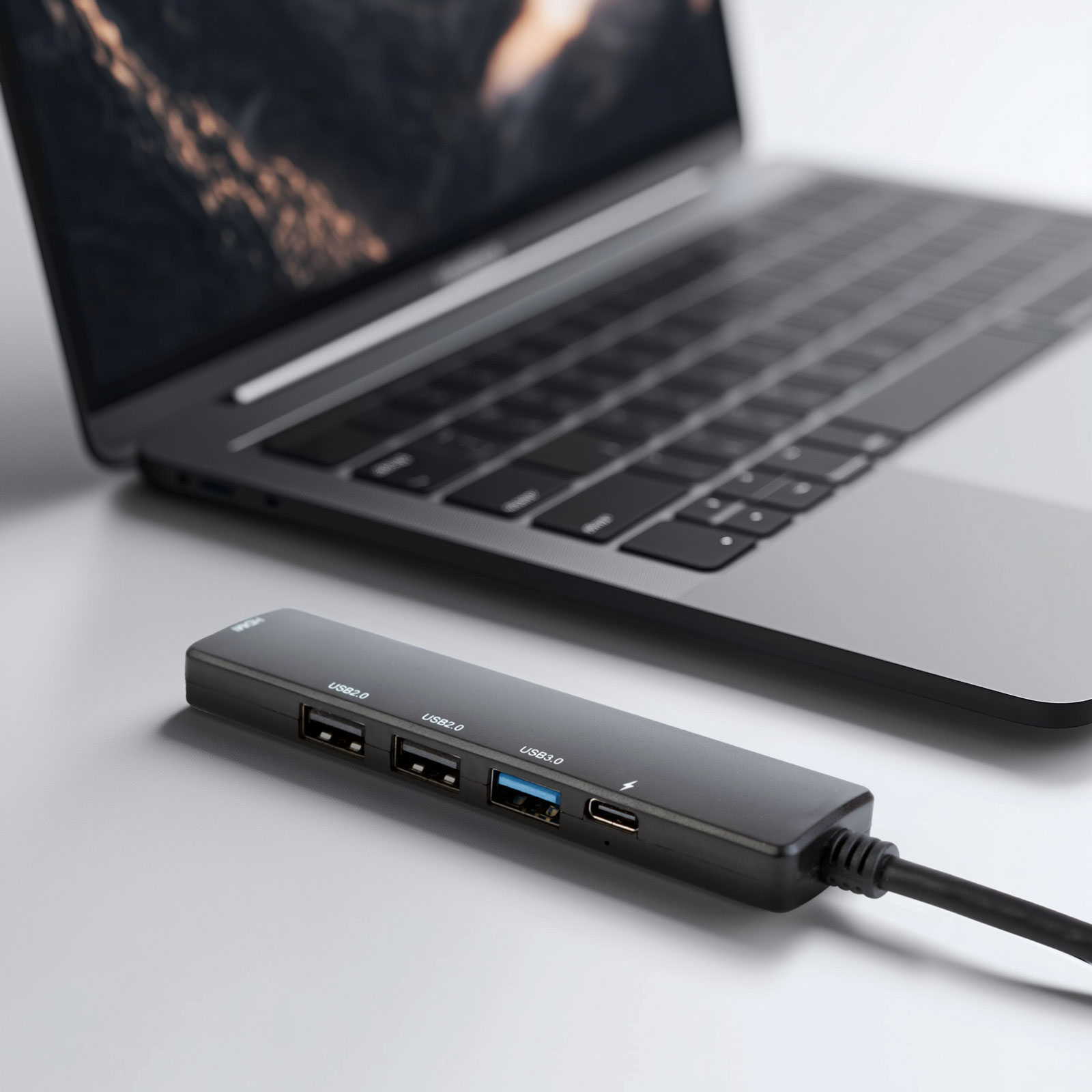 Fekete USB hub egy laptop mellett fehér felületen.