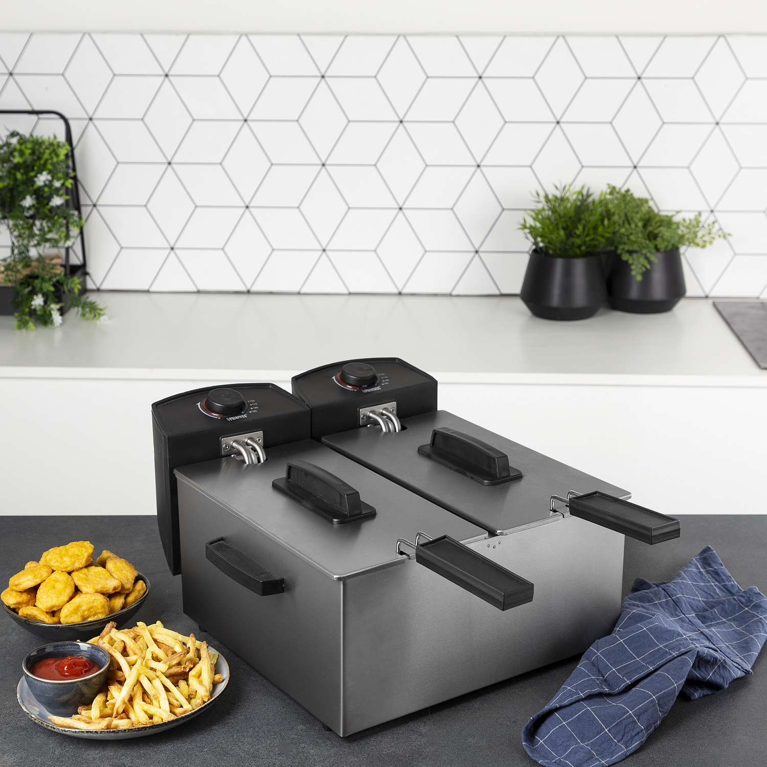 Friggitrice in acciaio inox a due sezioni. Patatine fritte e nuggets in ciotole vicine.