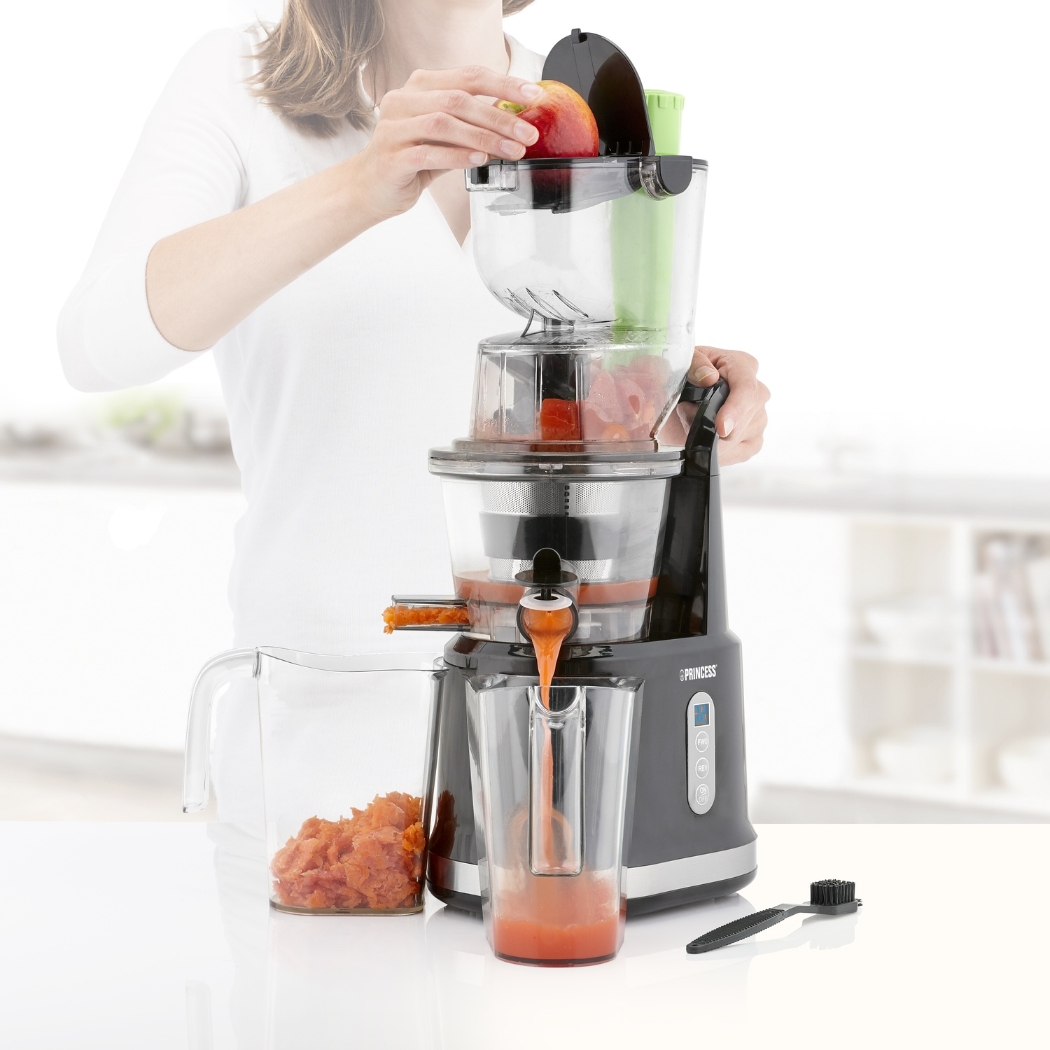 Una donna usa un estrattore. Sta mettendo una mela nella macchina. Una caraffa raccoglie il succo.