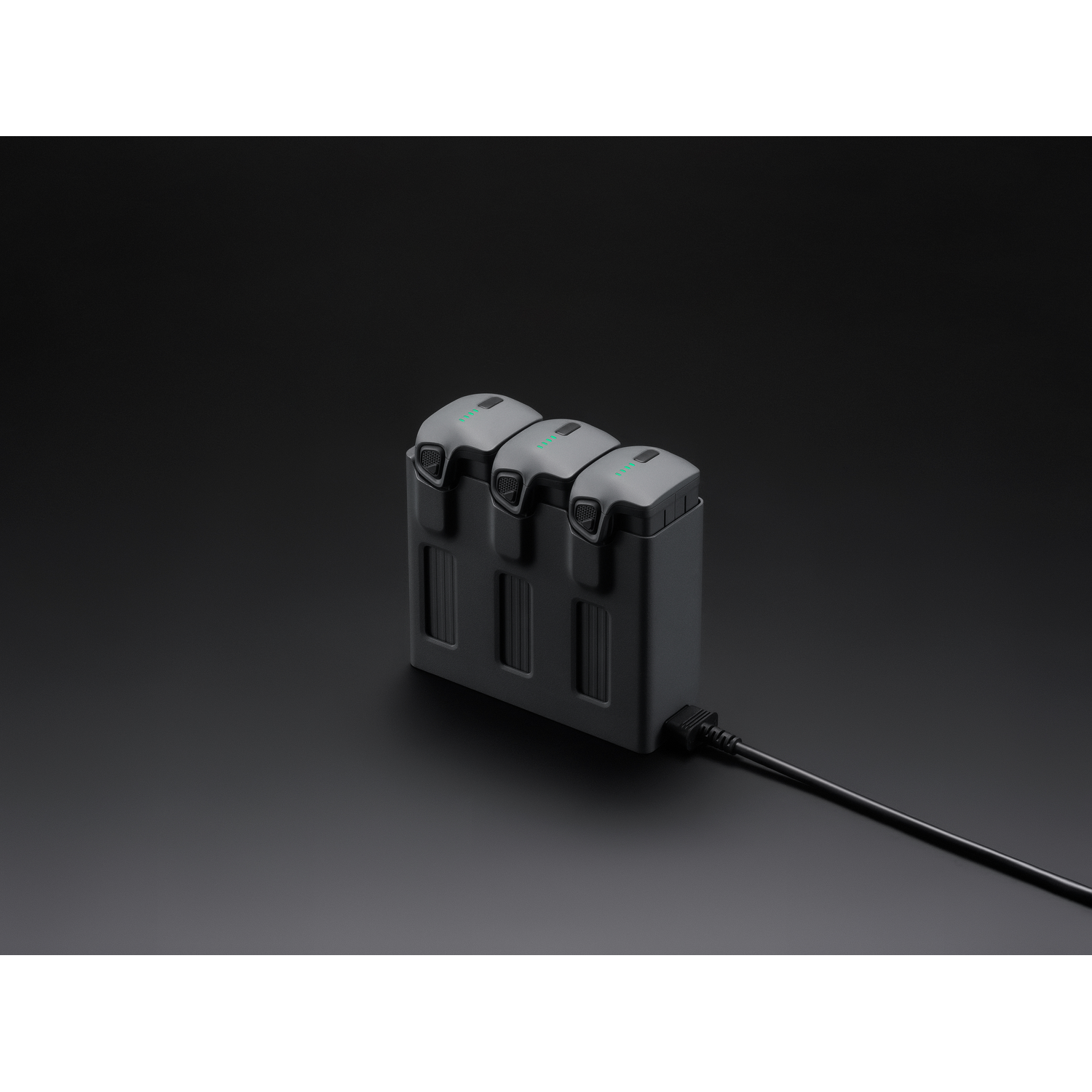 Three drone batteries are charging in a grey charging unit. Black background.