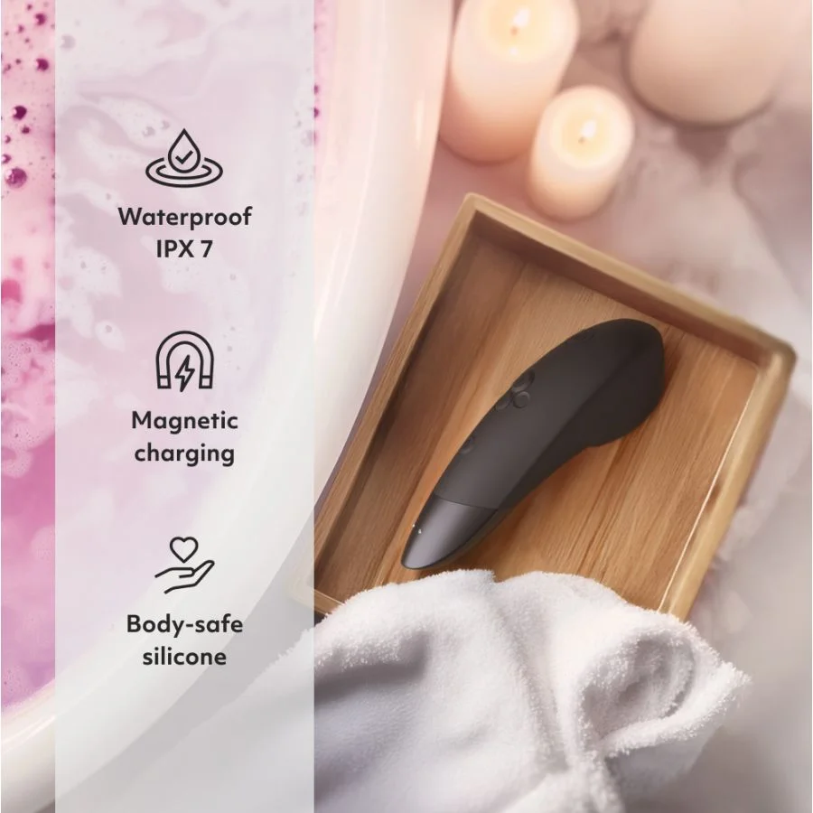 Un sex toy nero è su un vassoio di legno con un asciugamano bianco, vicino a un bagno con acqua rosa.