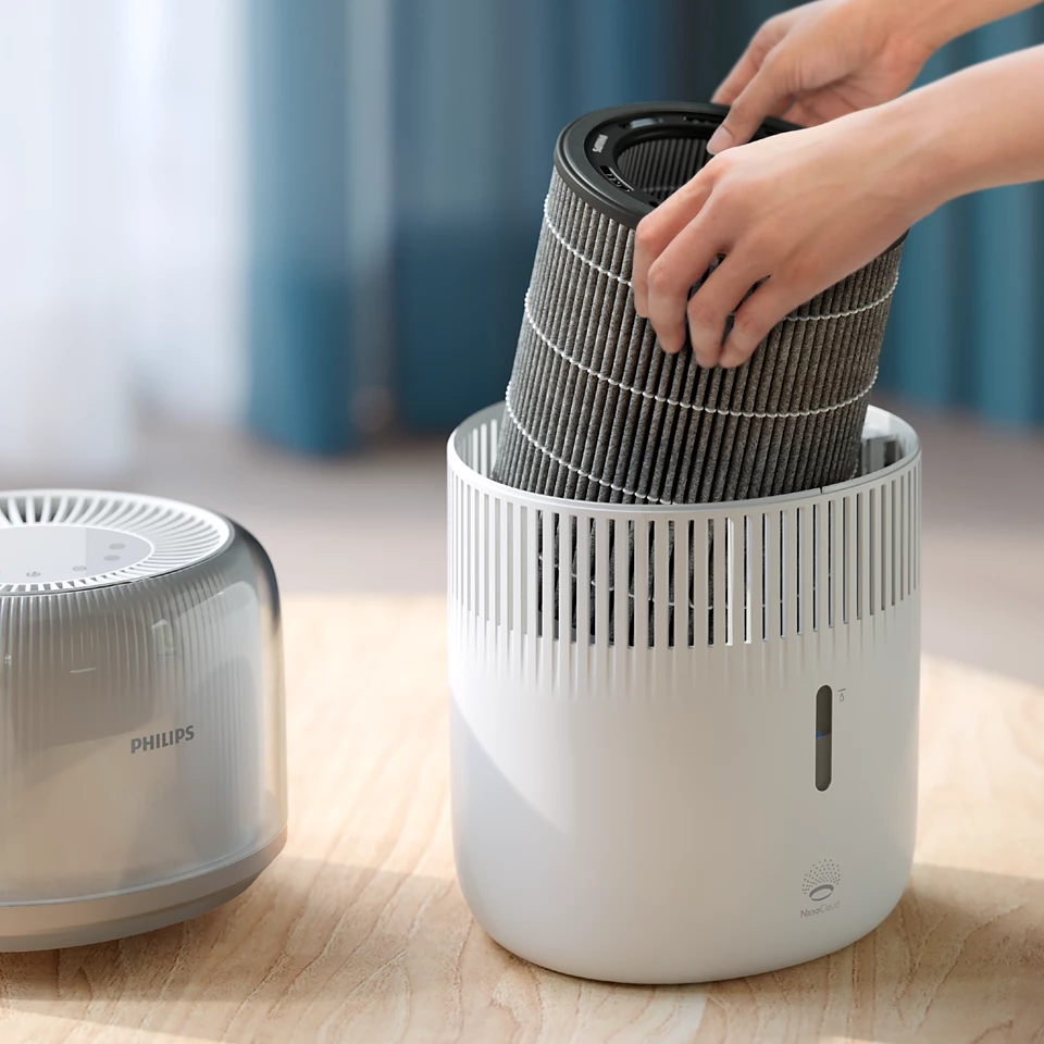 Kéz egy új szűrőt helyez egy fehér-szürke Philips légtisztítóba.