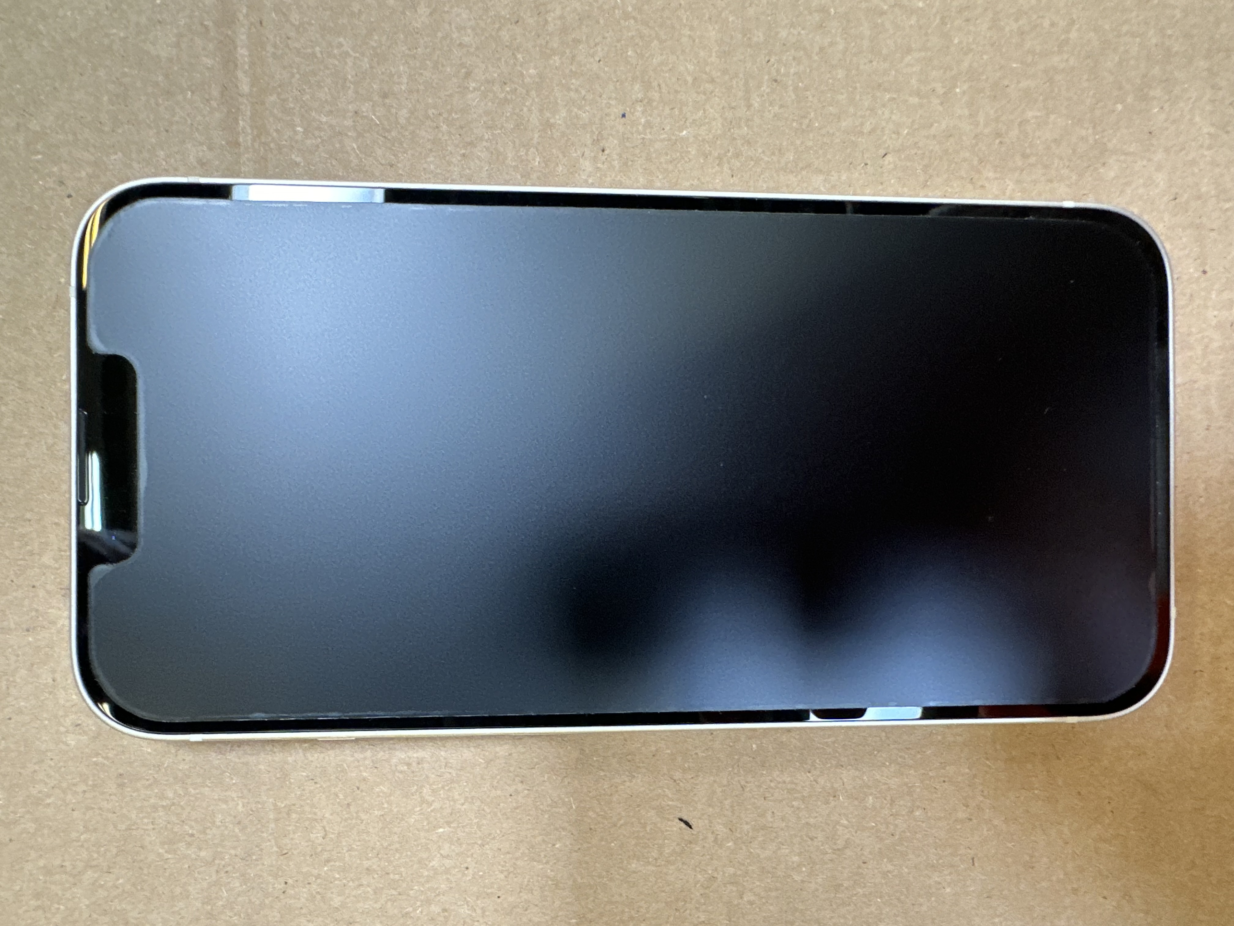 Czarny smartfon ze srebrną ramką, leżący na jasnobrązowej powierzchni. Ekran jest ciemny.