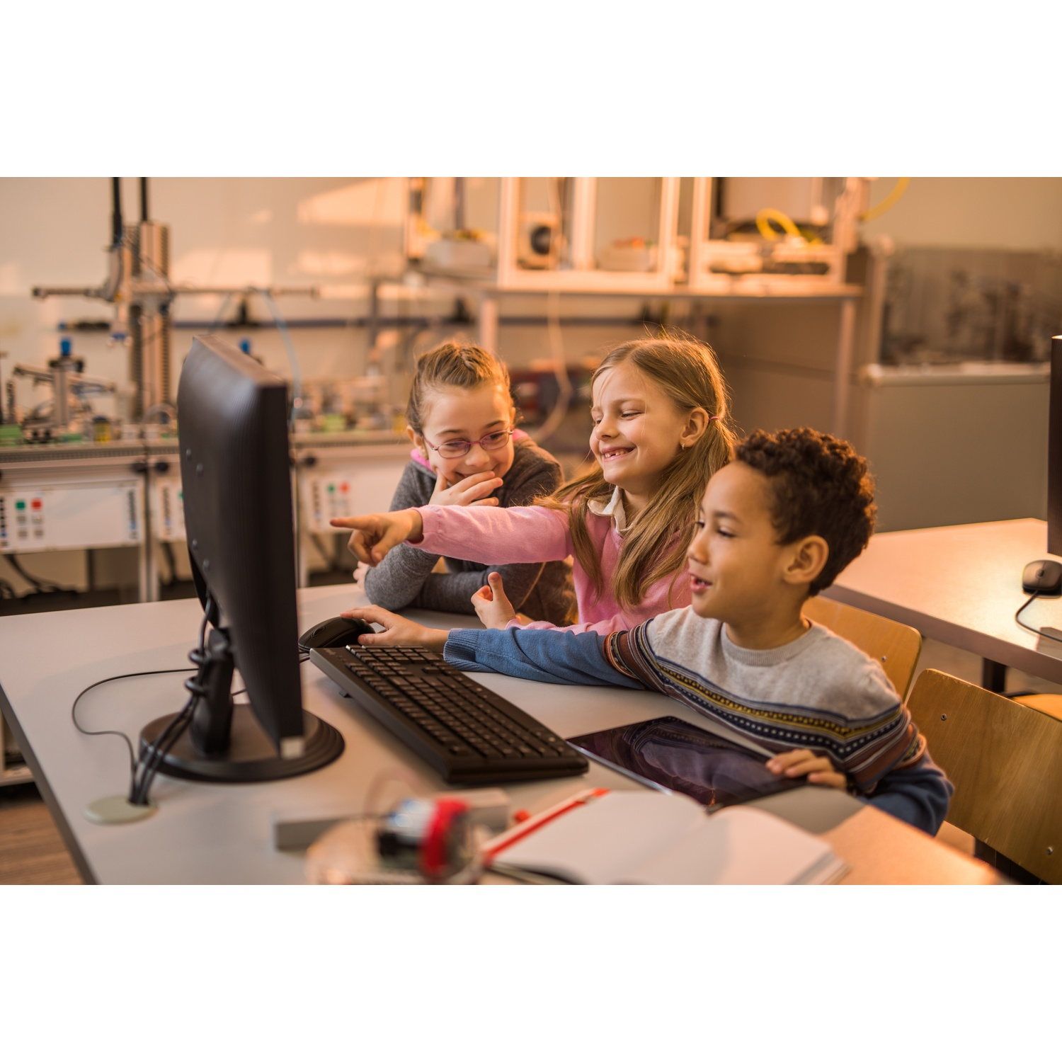 Tre bambini davanti a un computer, due che indicano lo schermo con sorrisi.