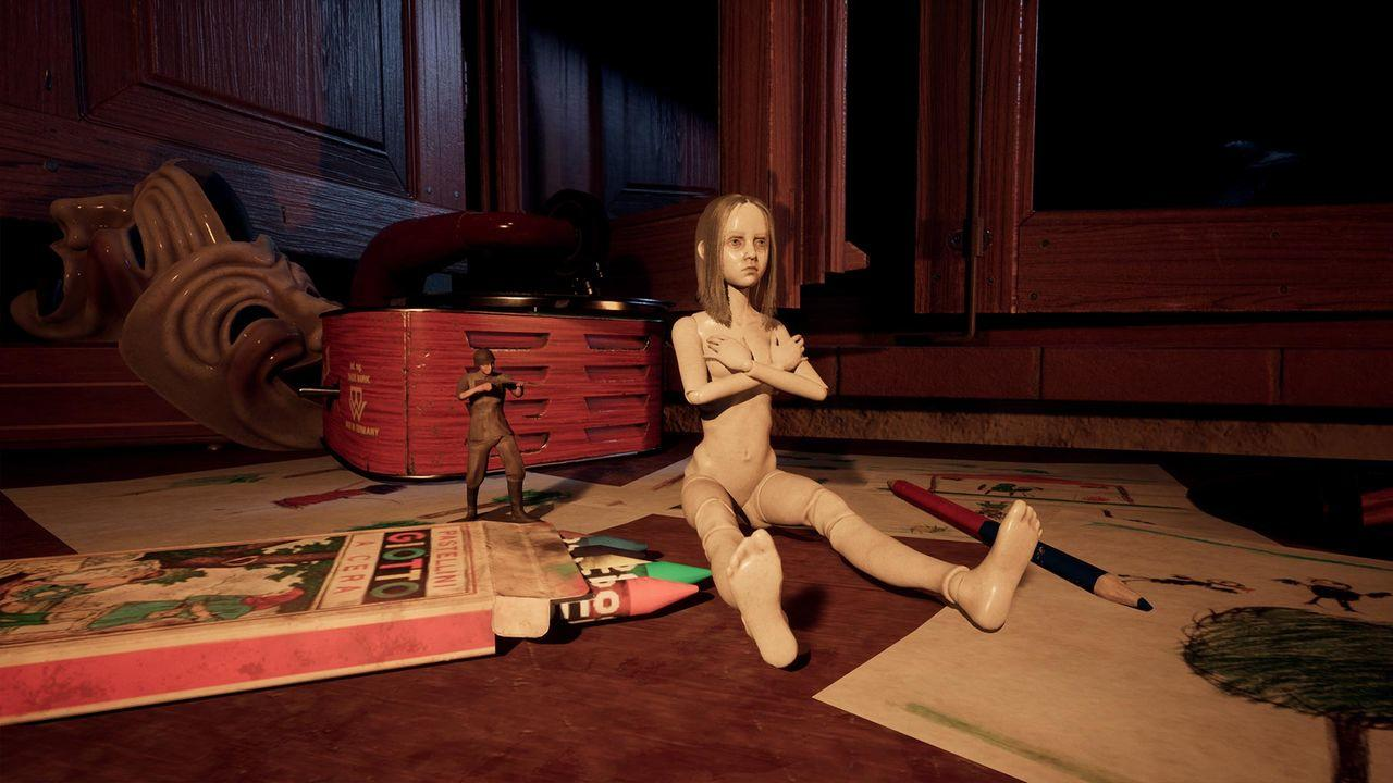 Eine Puppe und eine kleine Figur auf einem Tisch mit Buntstiften, einem Radio und einer Maske im Hintergrund.