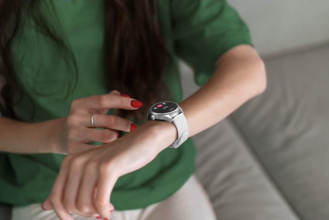 Eine Person mit einer Smartwatch, rotem Nagellack, überprüft den Bildschirm. Die Uhr hat ein weißes Armband.
