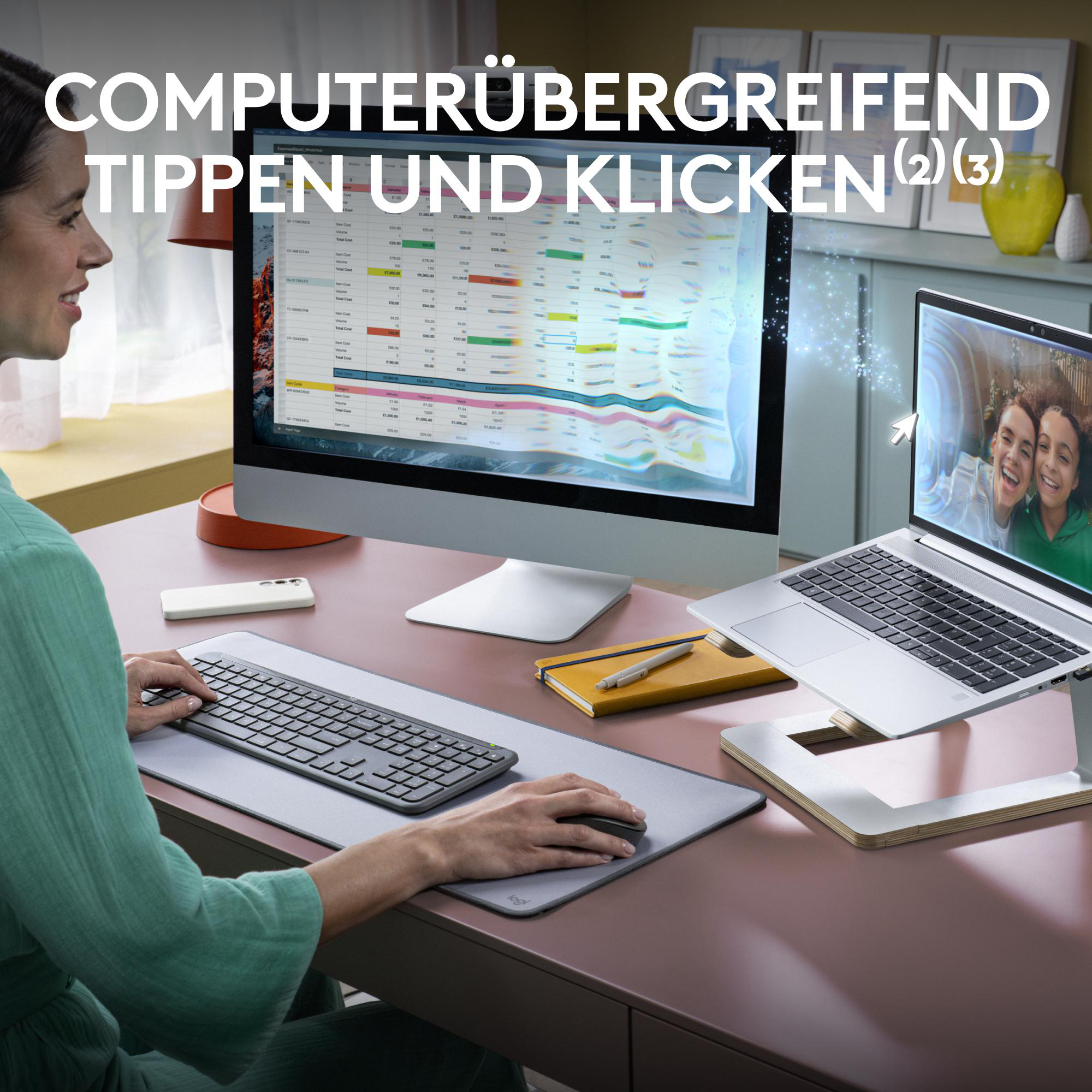 Eine Frau arbeitet an einem Computer, mit Laptop, Monitor, Tastatur und Zubehör auf einem Schreibtisch.