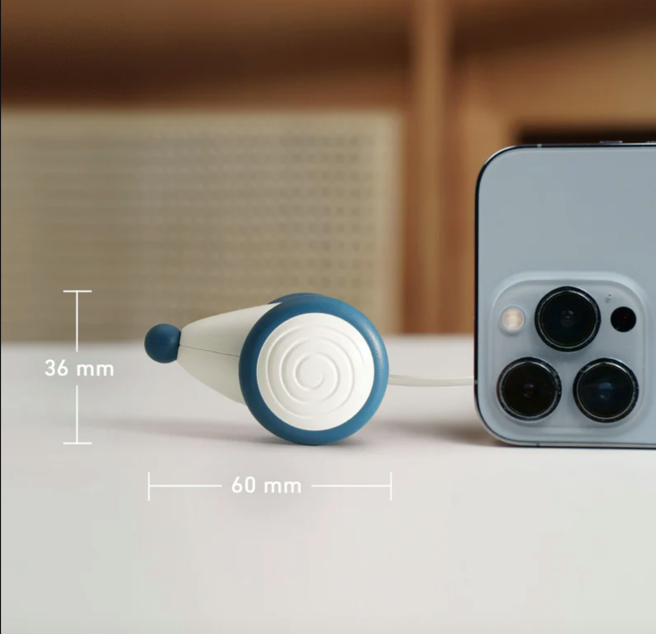 Ein weißer und blauer Kabelaufroller neben einem Smartphone. Abmessungen sind 36 mm und 60 mm.