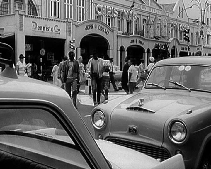 Ein Schwarz-Weiß-Foto einer Straßenszene mit Autos und Fußgängern.