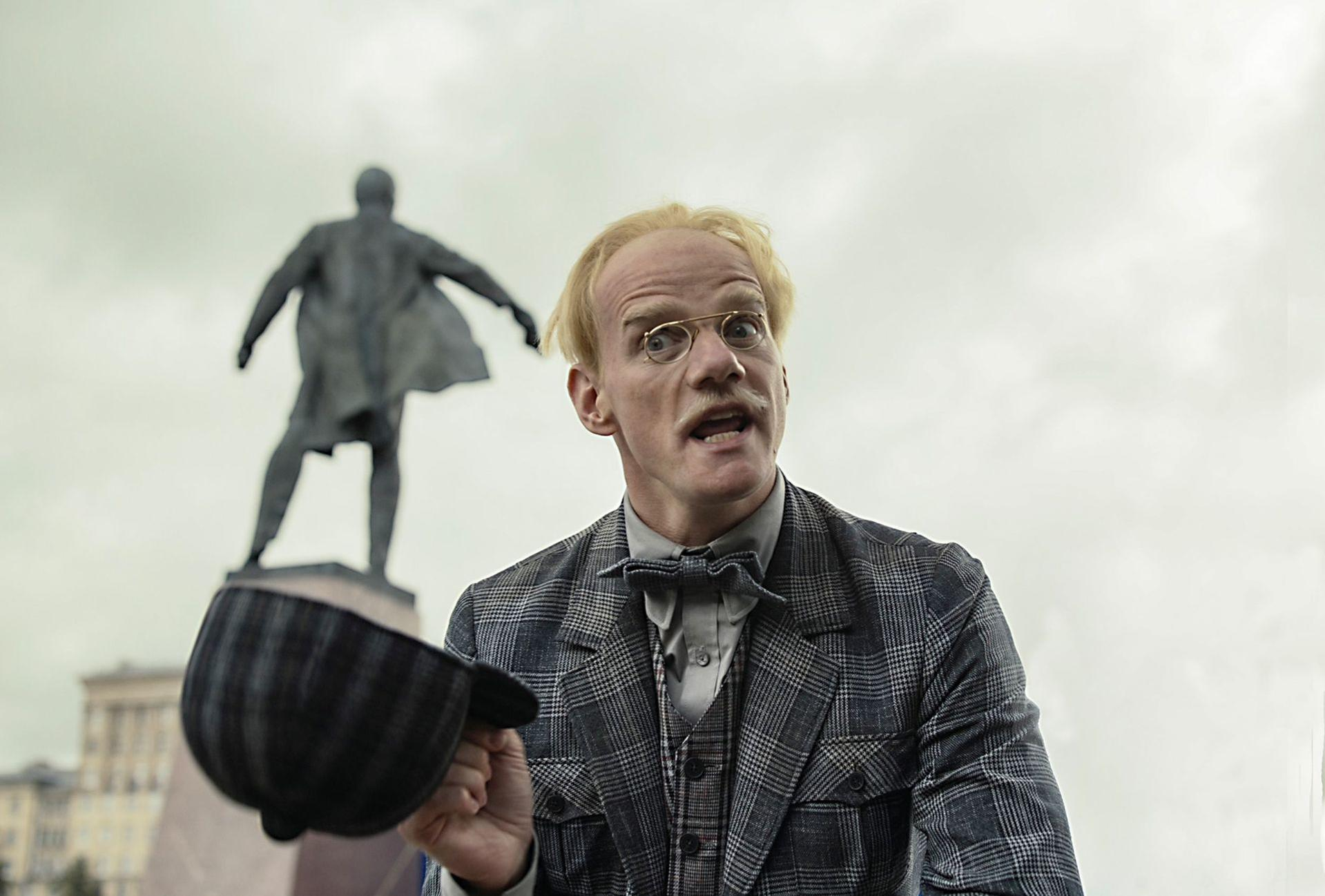 Ein Mann mit Hut hält einen Hut vor einer Statue.