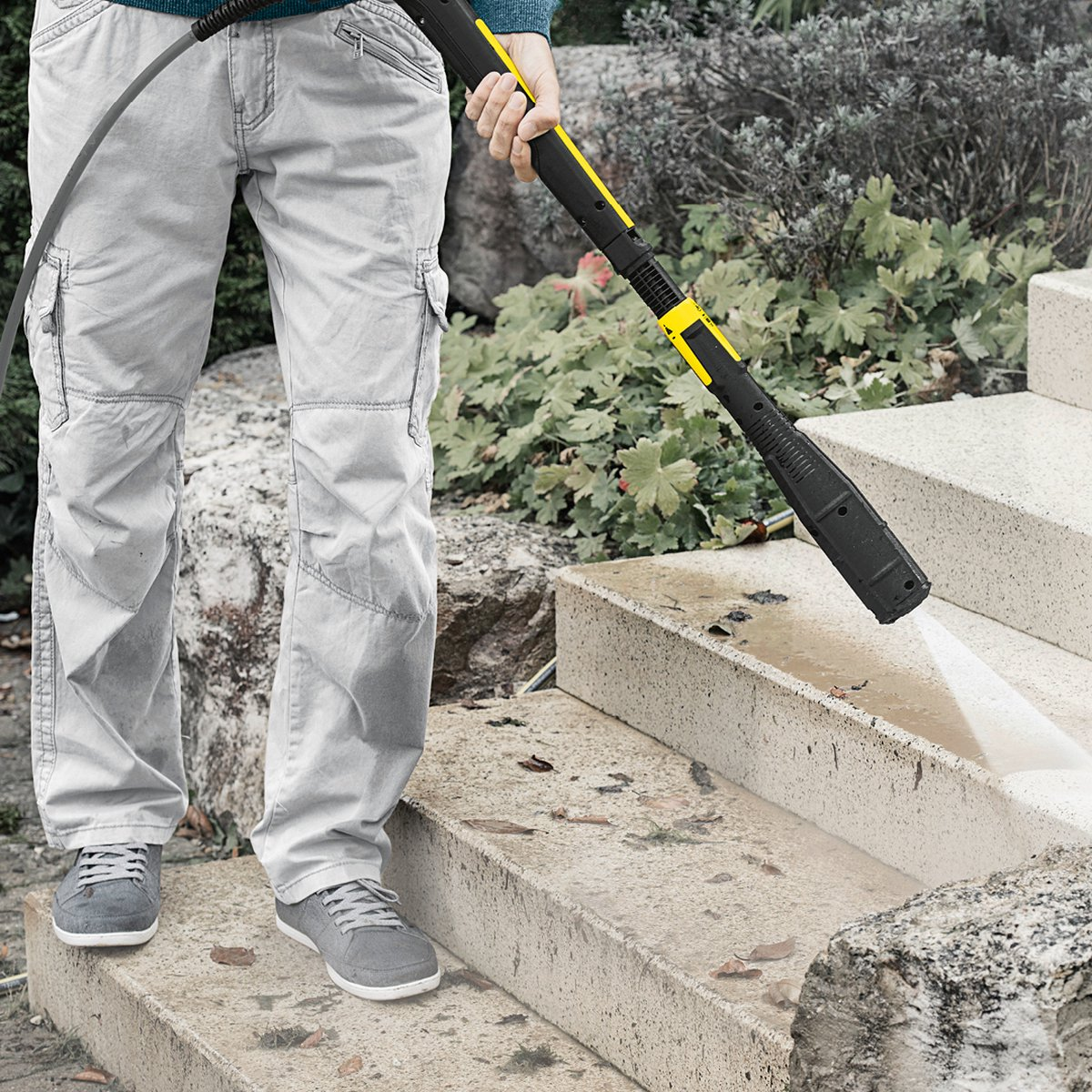 Osoba używa myjki ciśnieniowej do czyszczenia betonowych schodów.