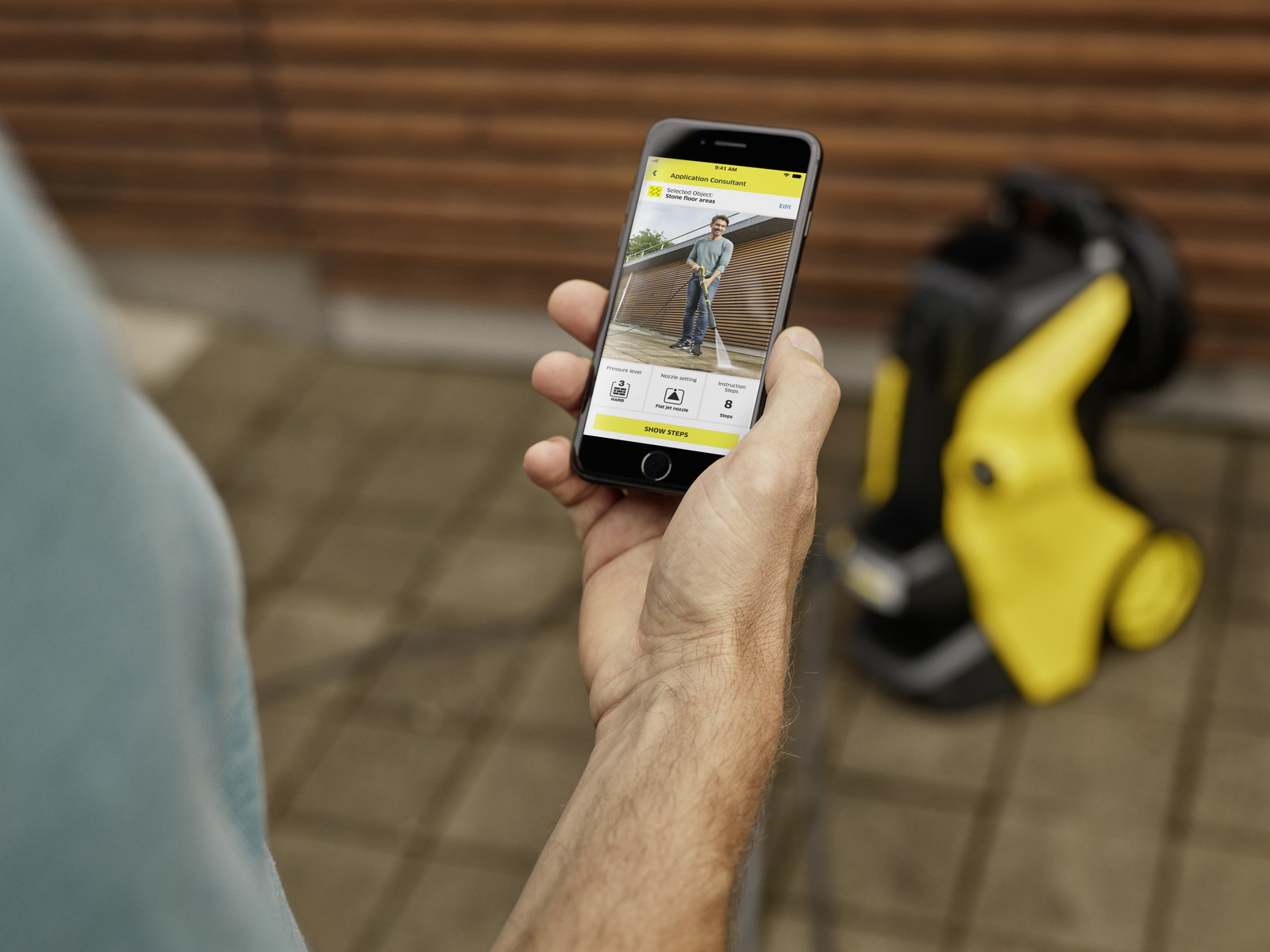 Osoba trzymająca telefon, pokazująca obraz mężczyzny używającego myjki ciśnieniowej.