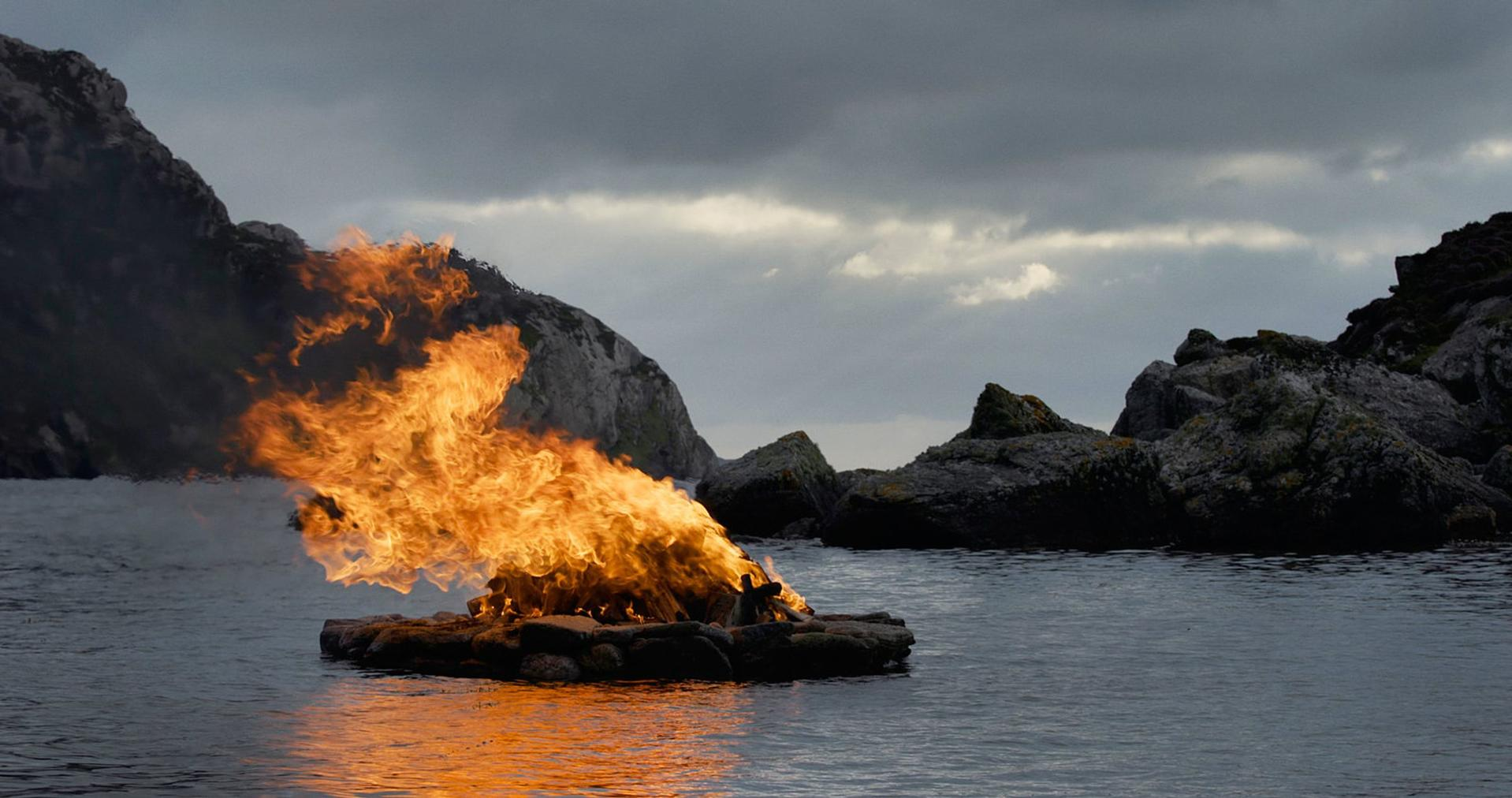 Feuer auf Wasser, Felsen im Hintergrund, dunkler Himmel.