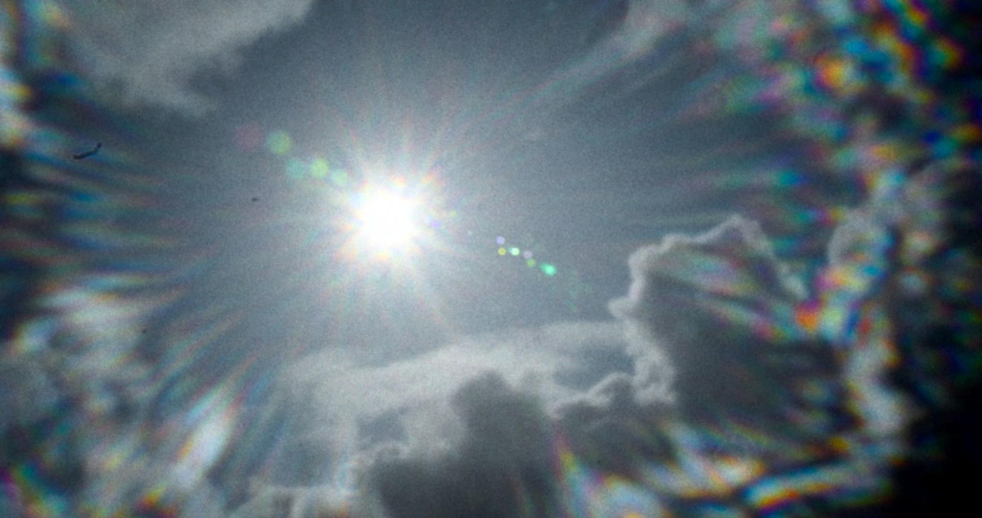 Helle Sonne in einem bewölkten Himmel, mit Linsenreflexen.