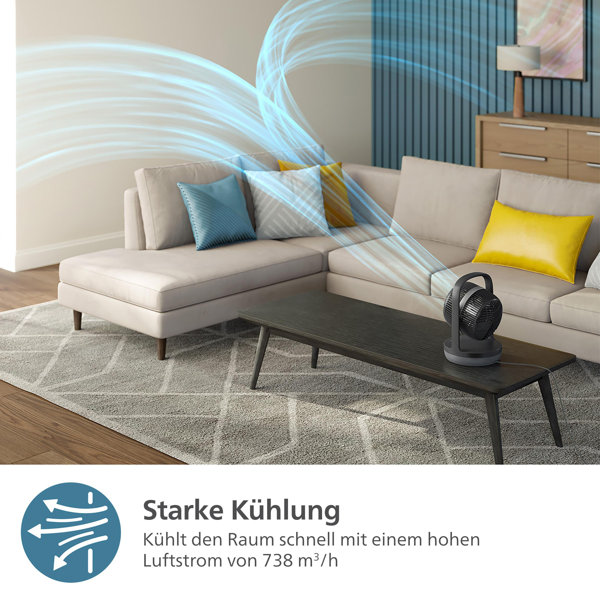 Wohnzimmer mit Ventilator auf einem Tisch. Sofa und Kissen im Hintergrund.