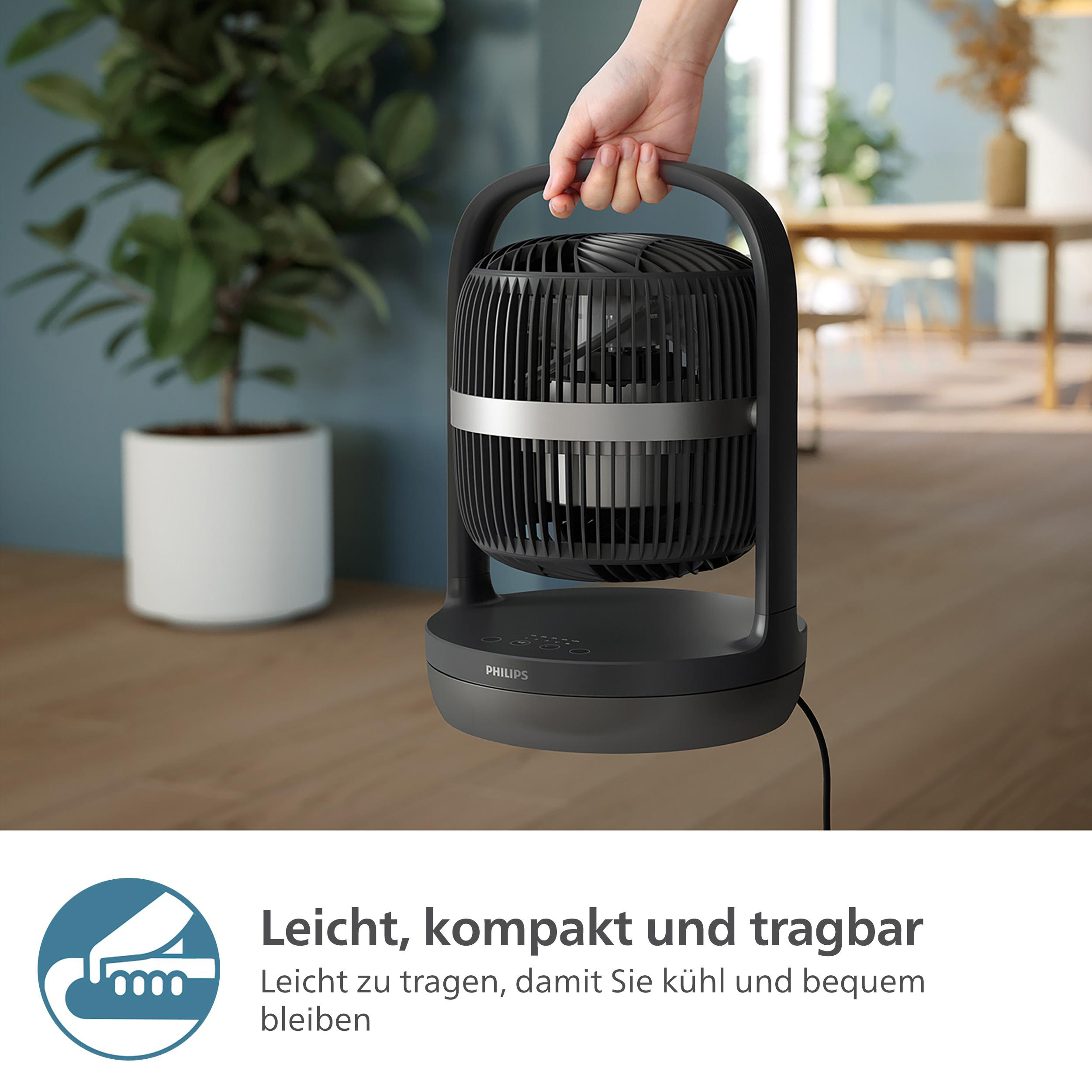 Ein schwarzer Ventilator mit Griff, gehalten von einer Hand. Eine Pflanze im Hintergrund.